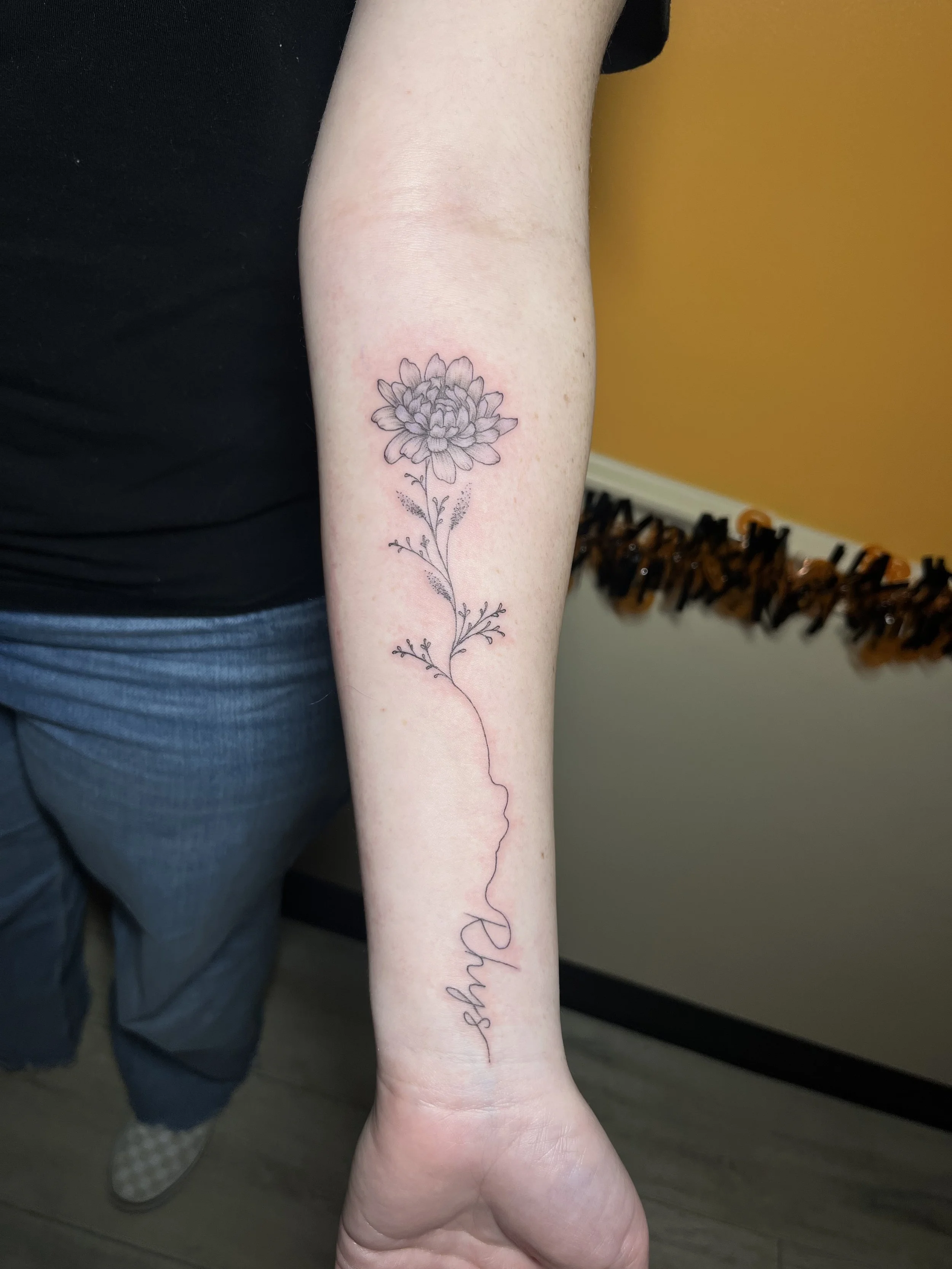 A person's inner forearm tattoo of a detailed flower with a long, winding stem and the word 'Relax' written in cursive underneath.