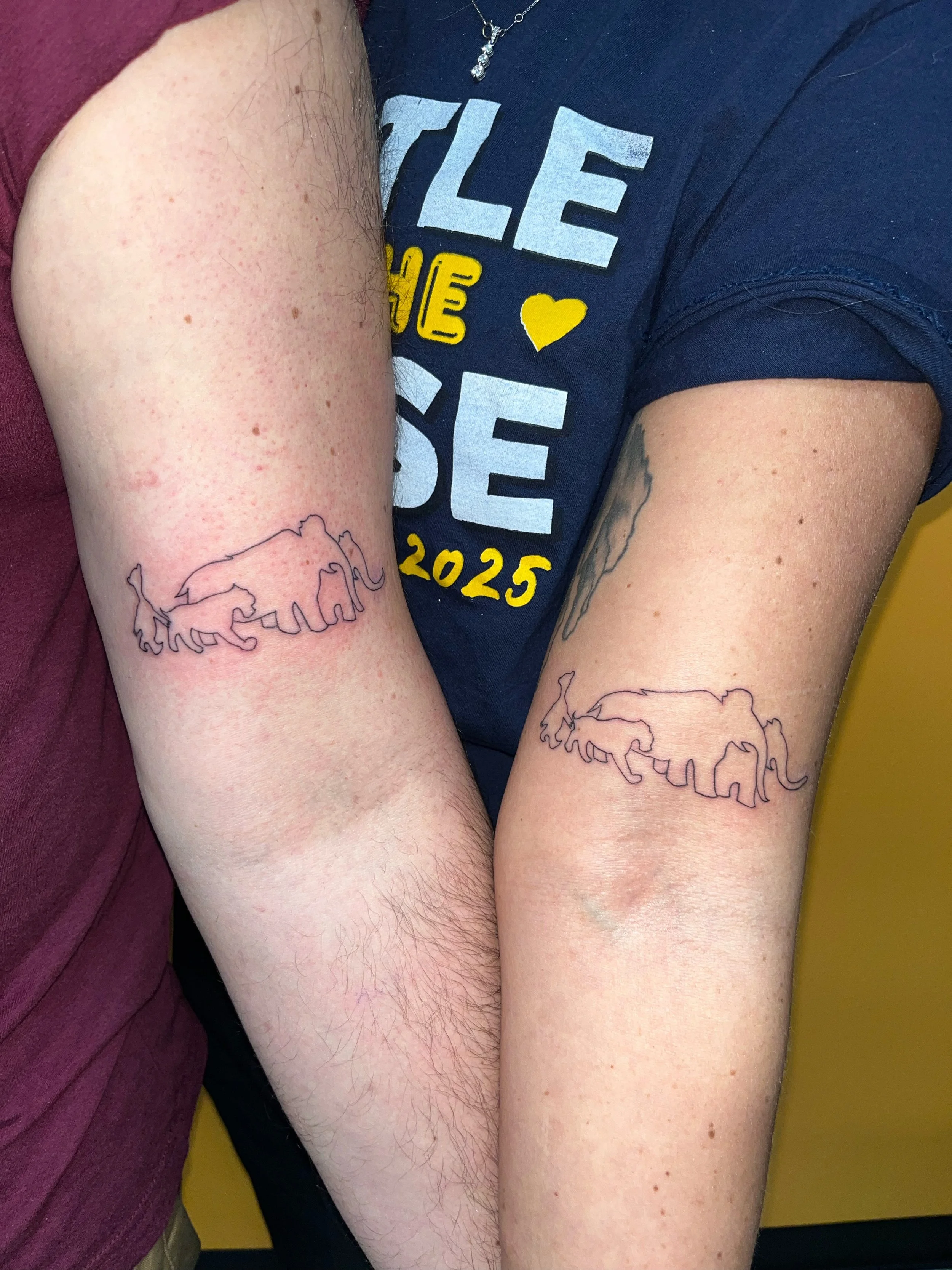 Two people show matching tattoos of outlines of elephants and rhinoceroses on their upper arms.