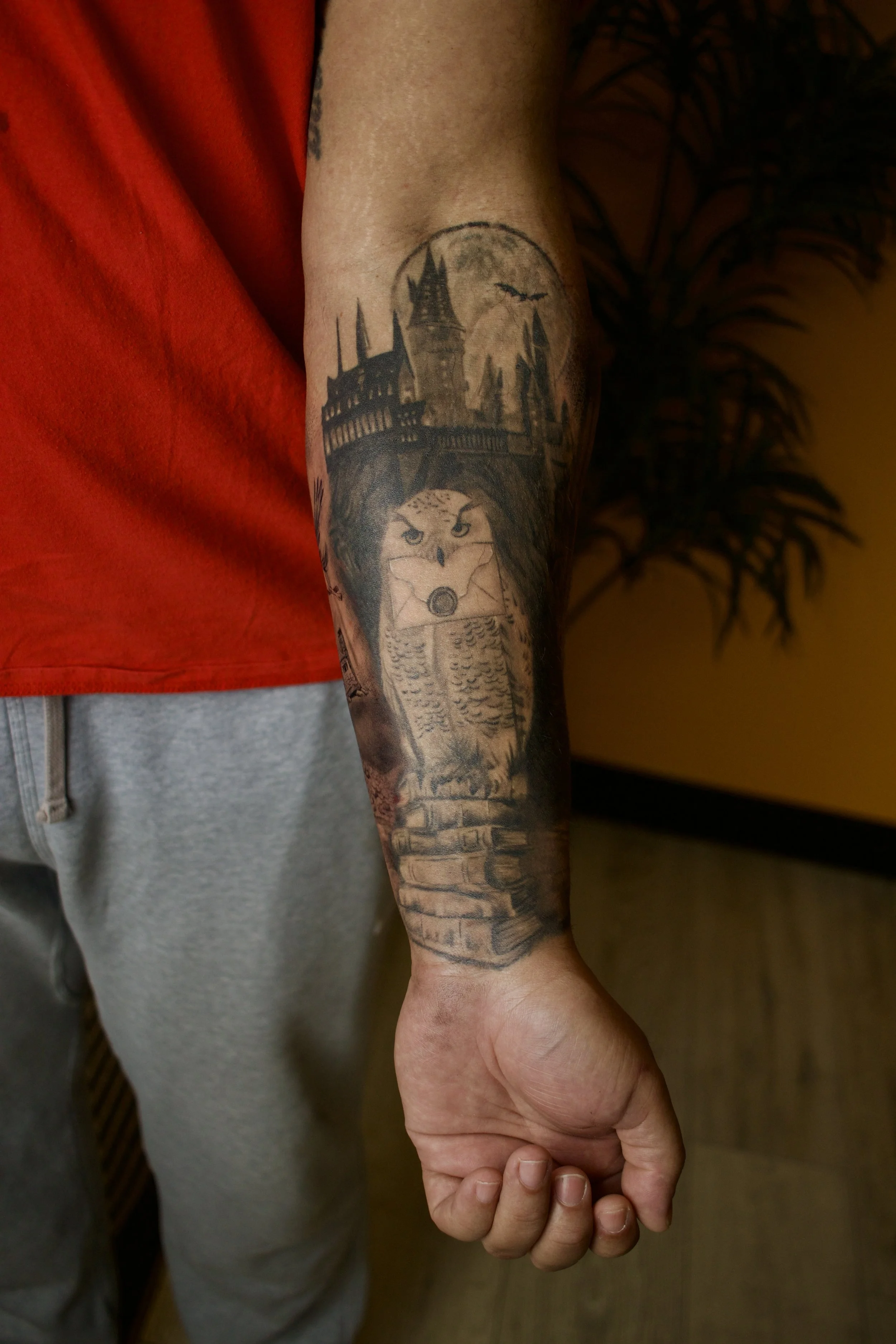 Tattoo of an owl on a person's forearm, with a castle, bridge, and moon in the background.
