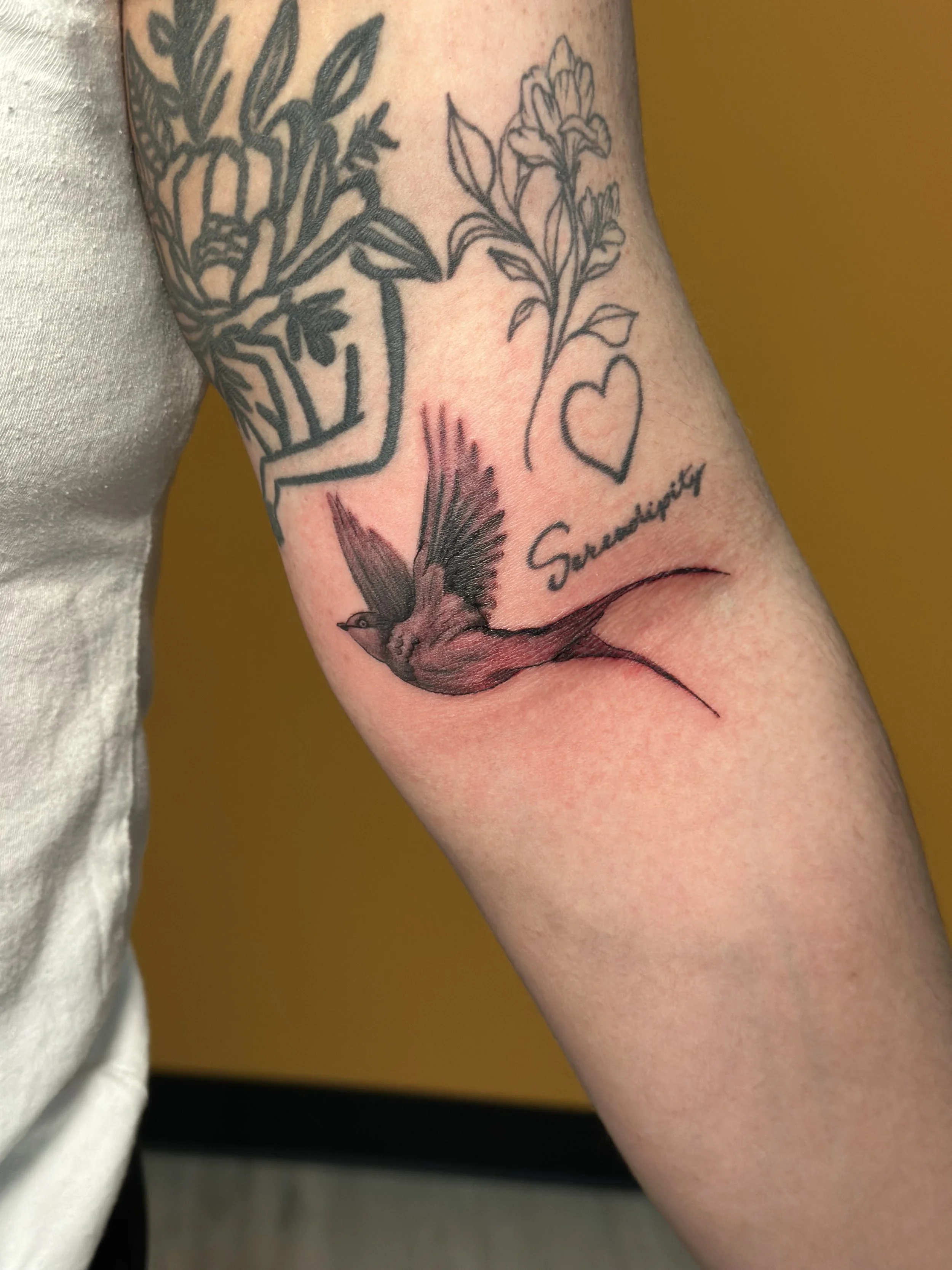 Tattoo on a person's arm featuring a flying bird, a flower, a heart, and the word 'Sincerity' written in cursive.