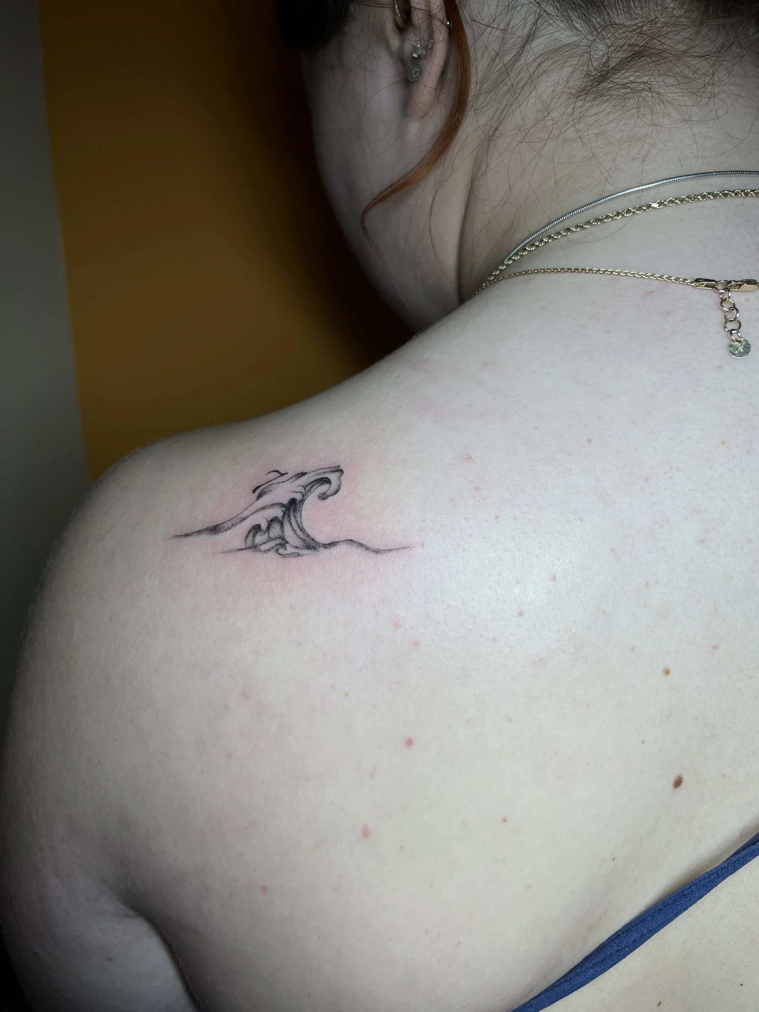 Close-up of a person's shoulder with a tattoo of ocean waves.