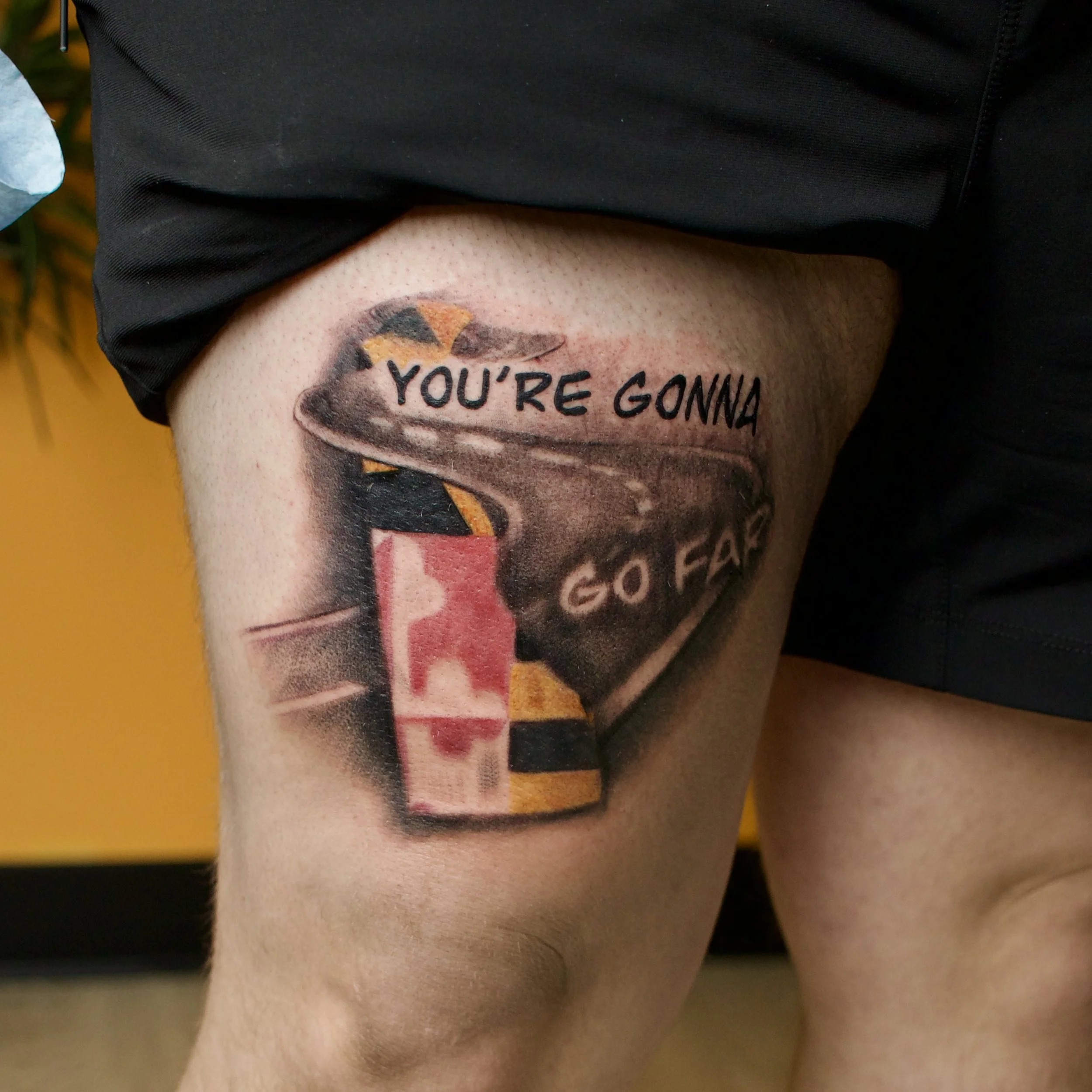 Tattoo of a can with a red, pink, and white pattern and a burning cigarette inside, with the words "YOU'RE GONNA GO FAR" above it.