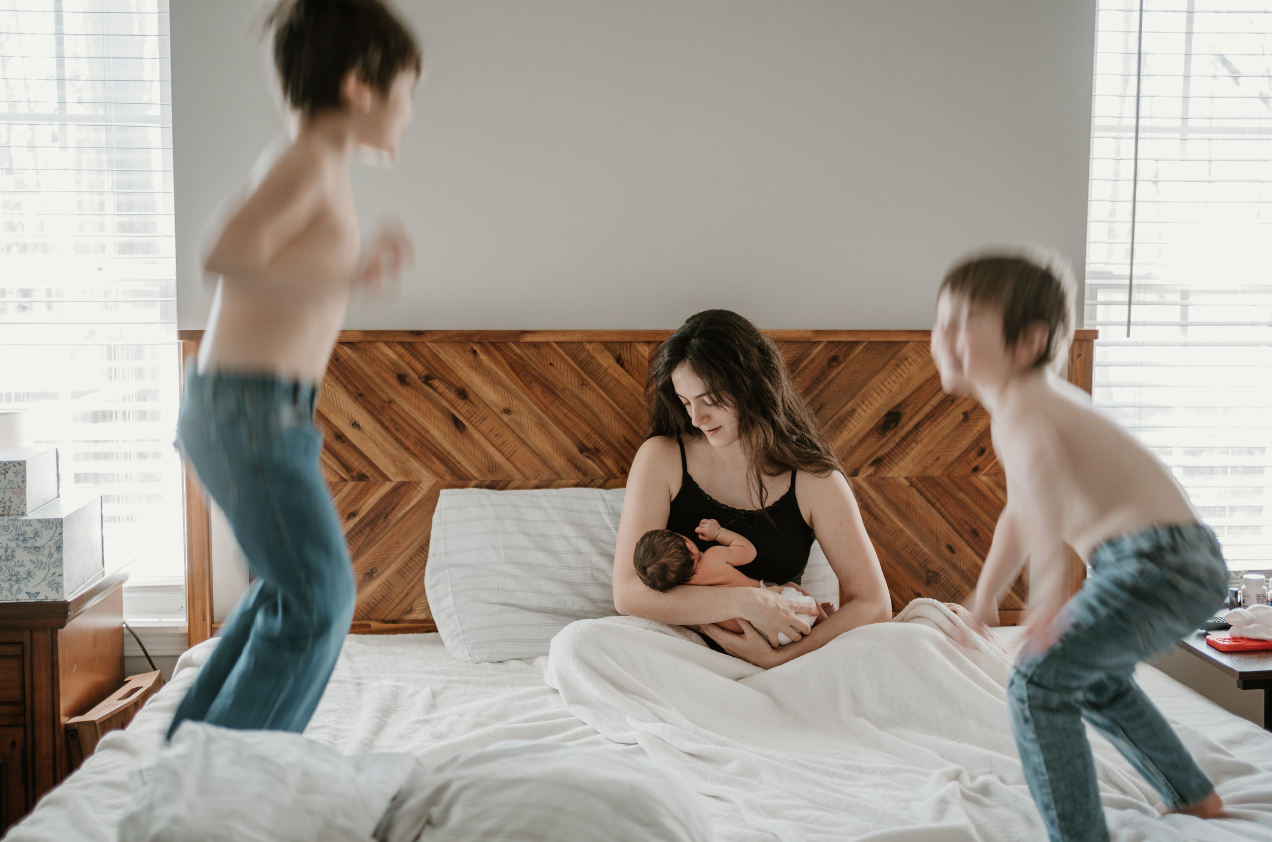 toddler boys jumping on bed while mom is nursing fresh baby