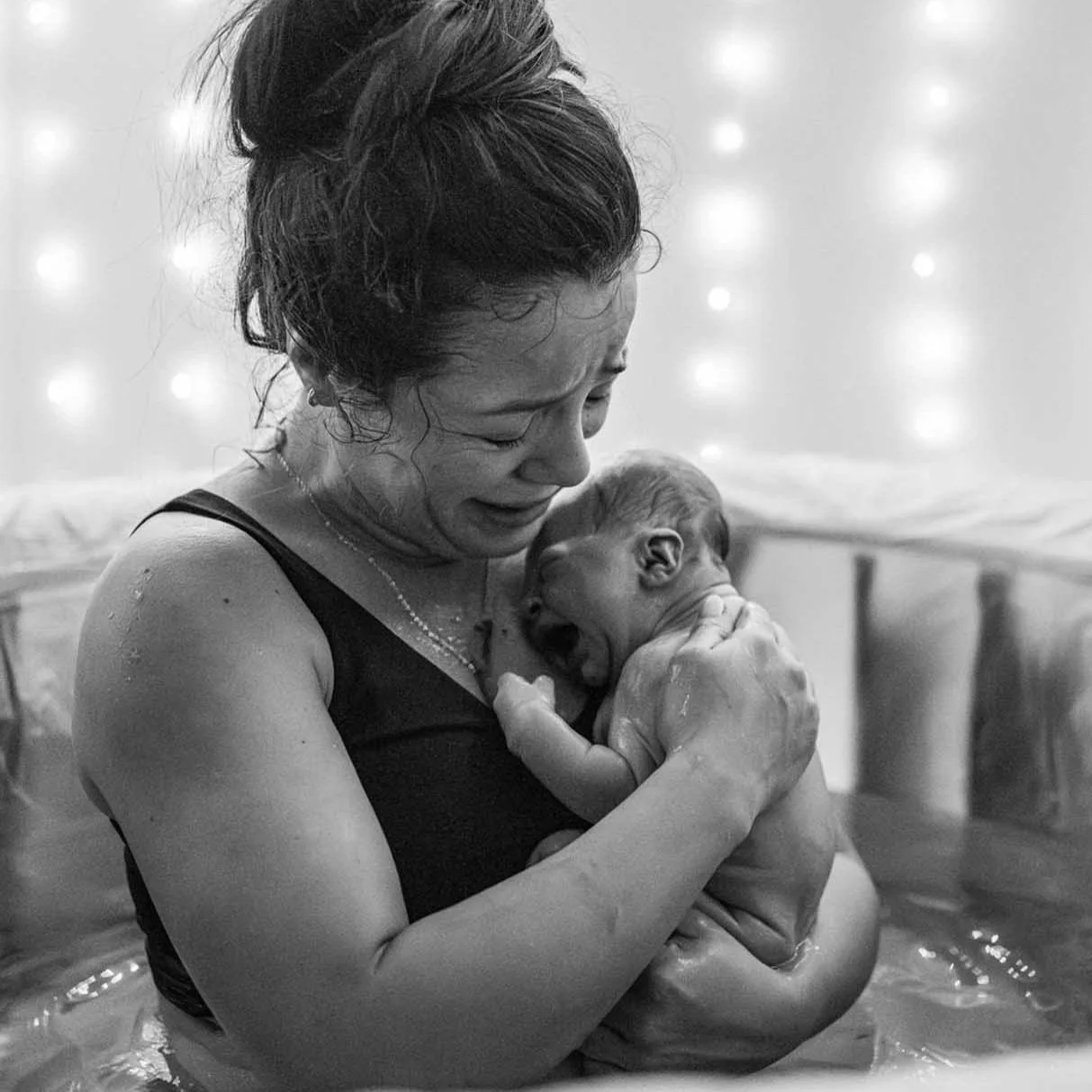 mother holding newborn baby in birth pool moments after birth