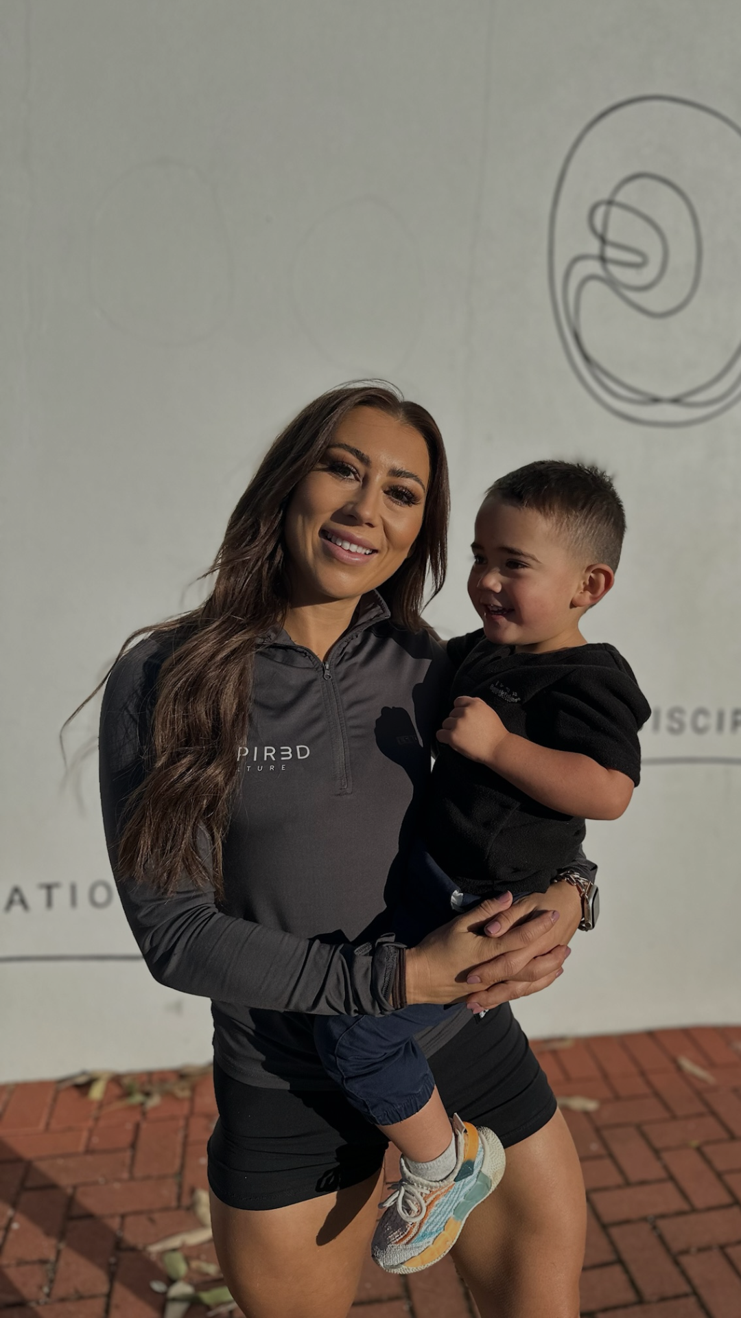 Woman holding a smiling child against a wall with a drawing in the background.