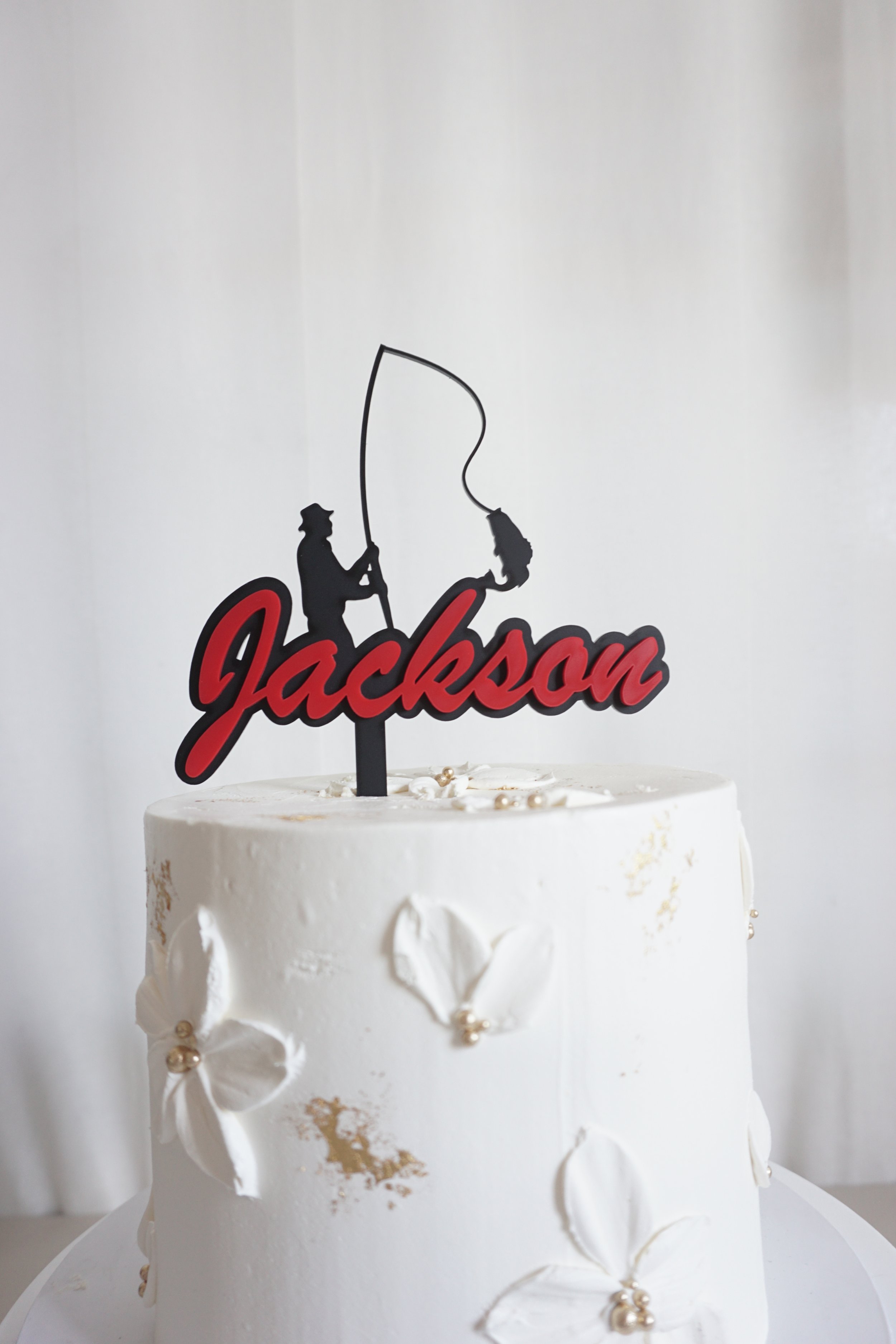 A custom fishing cake topper featuring a fisherman and a fish. Name says Jackson in red but that can be changed