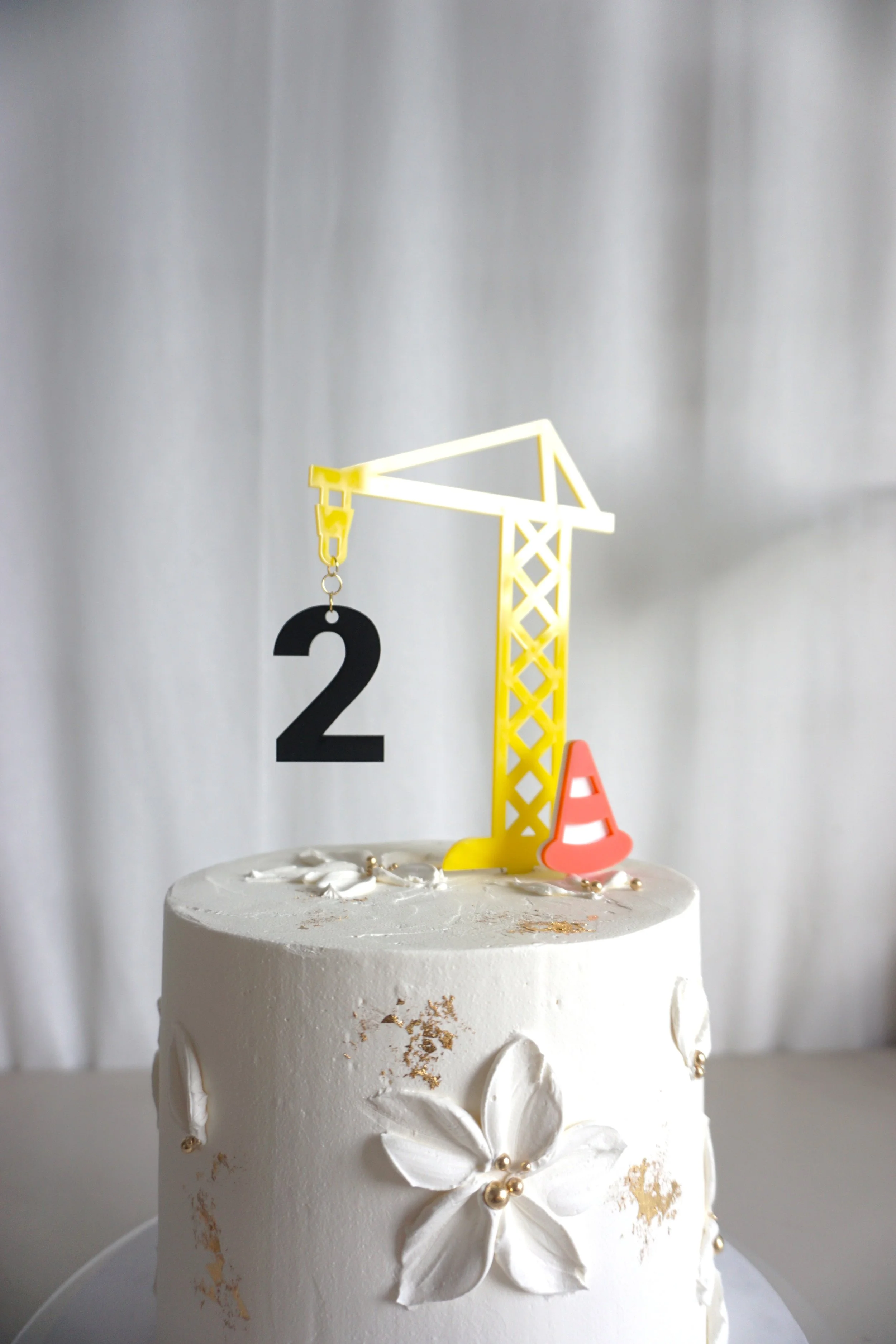 A crane cake topper with a hanging 2 and a safety cone.