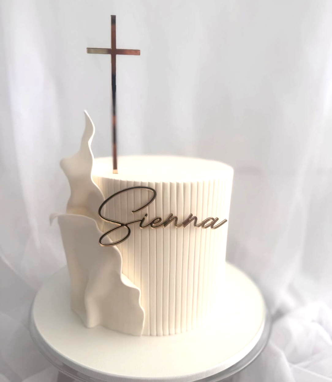 A white fondant cake with a gold Sienna fropper on the front with a gold mirror cross on the top. Designed and decorated by Faye Cahill