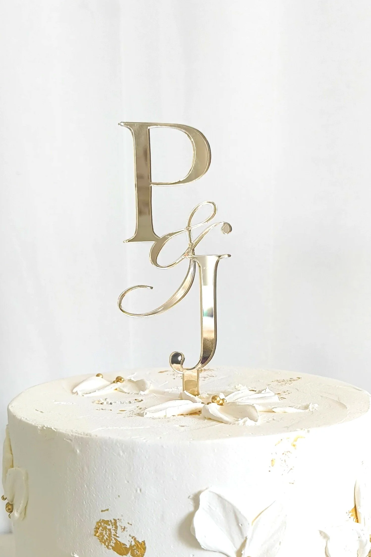 A gold mirror cake topper made into a monogram style featuring the characters P&J. Customised for a wedding cake
