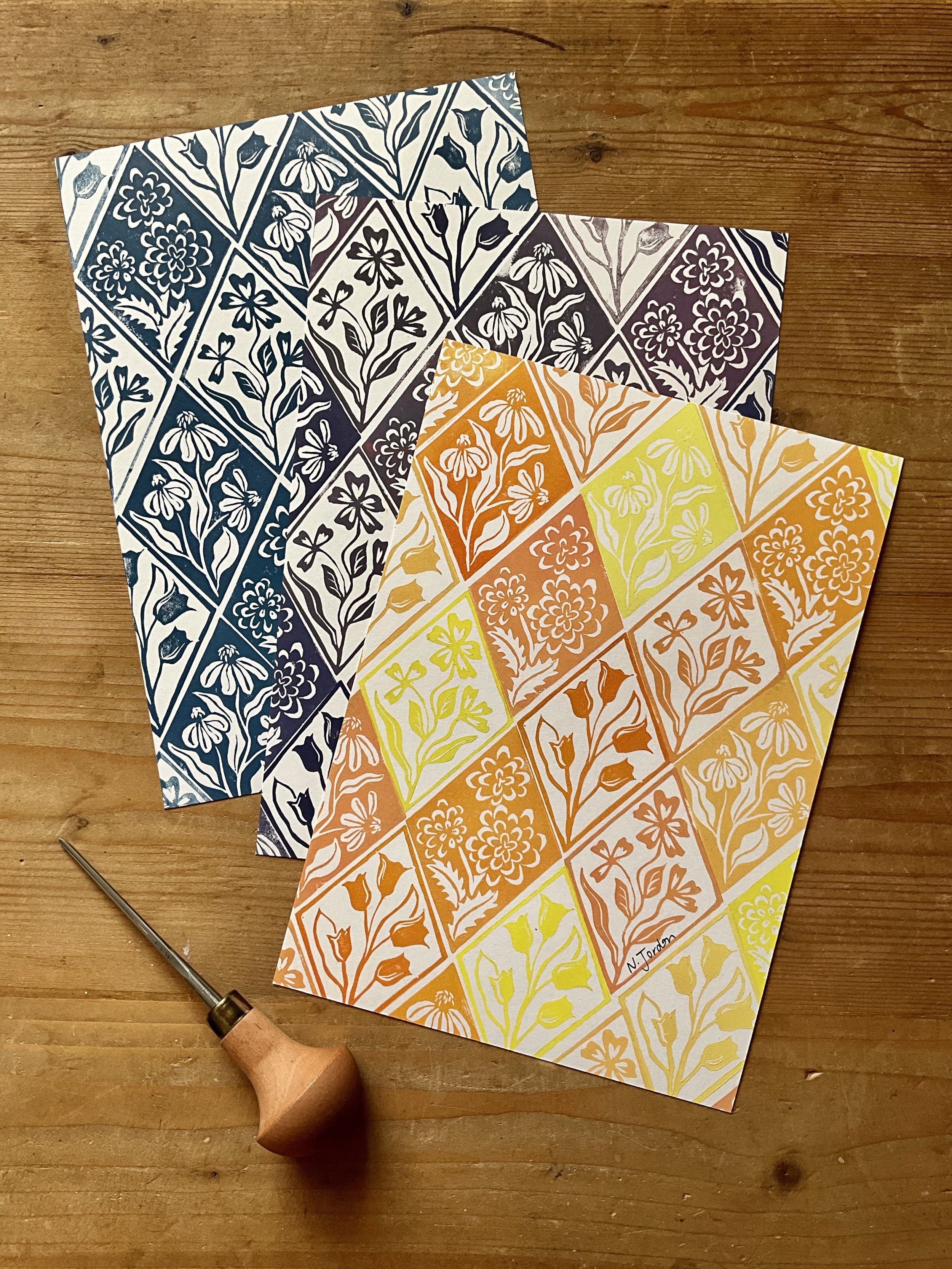 Floral diamonds original lino cut prints, in A5. Three prints shown here, in blue, purple and yellows/oranges. Photo shows lino carving tool too.