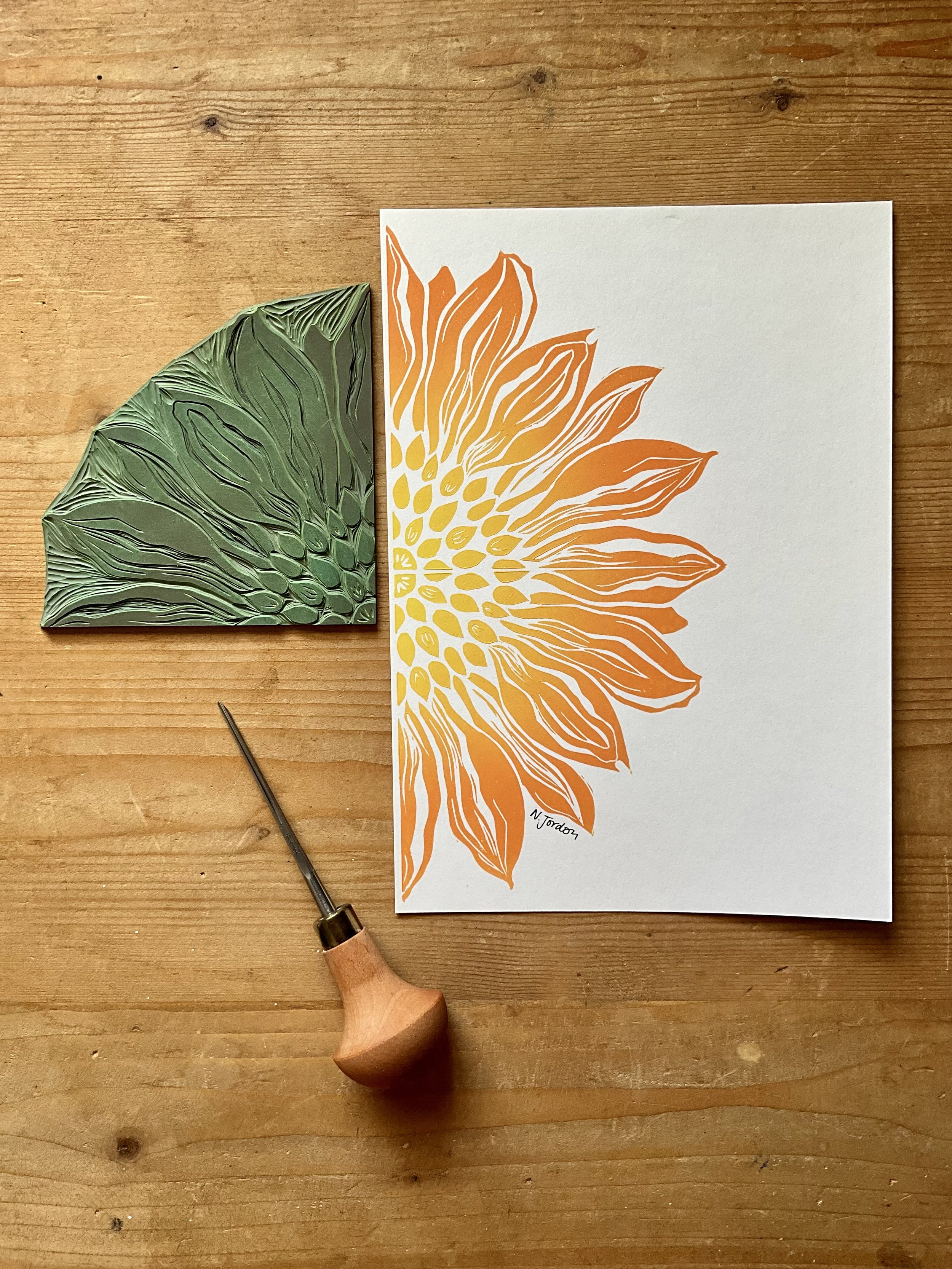 Sunflower original lino cut print, in A5. Hand printed in orange-yellow ombré. Photo also shows lino carving tool and the sunflower block used to print this piece.