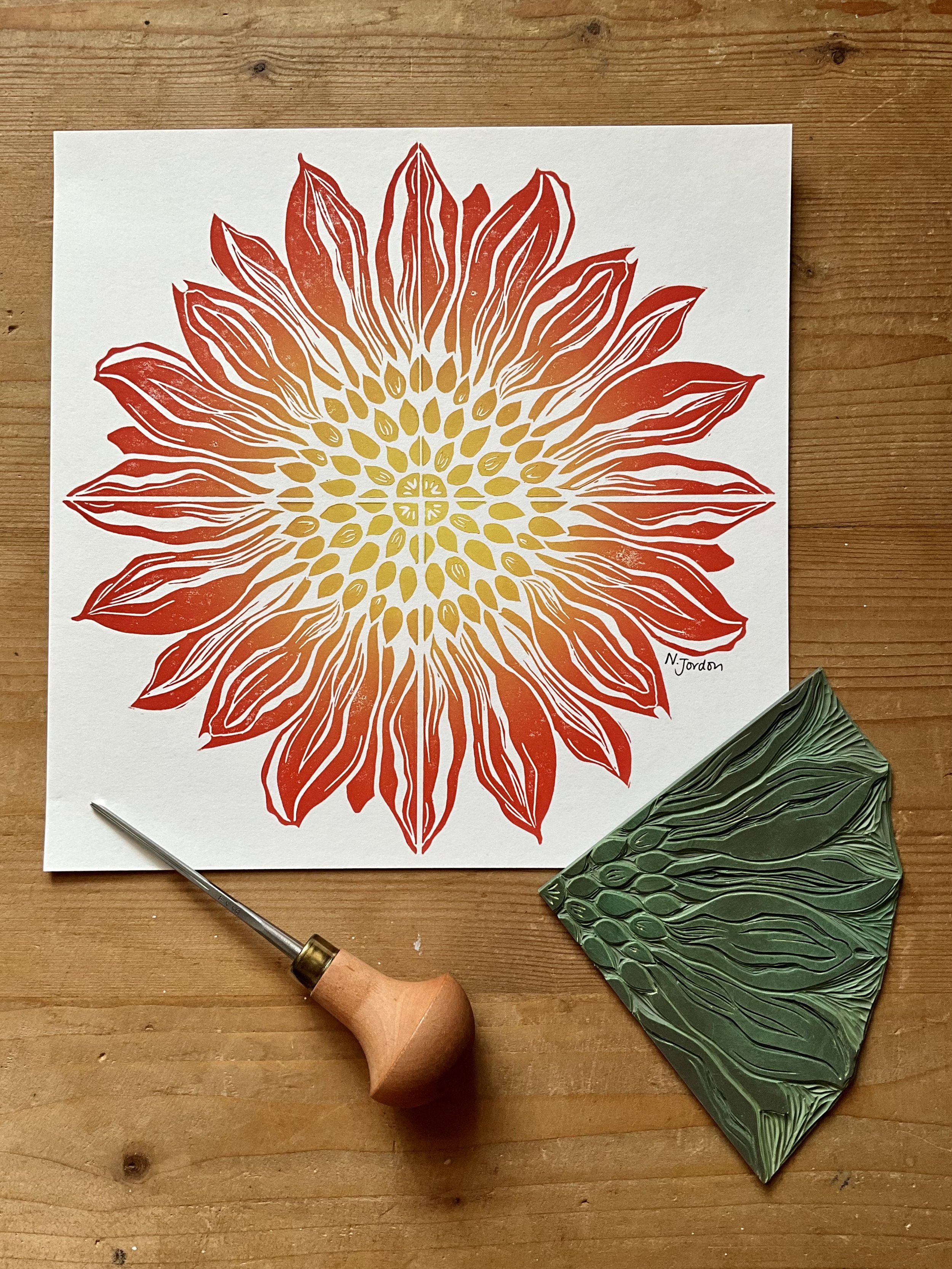 Full sunflower original lino cut print, in A4. Hand printed in red-yellow ombré. Photo also shows lino carving tool and the sunflower block used to print this piece.