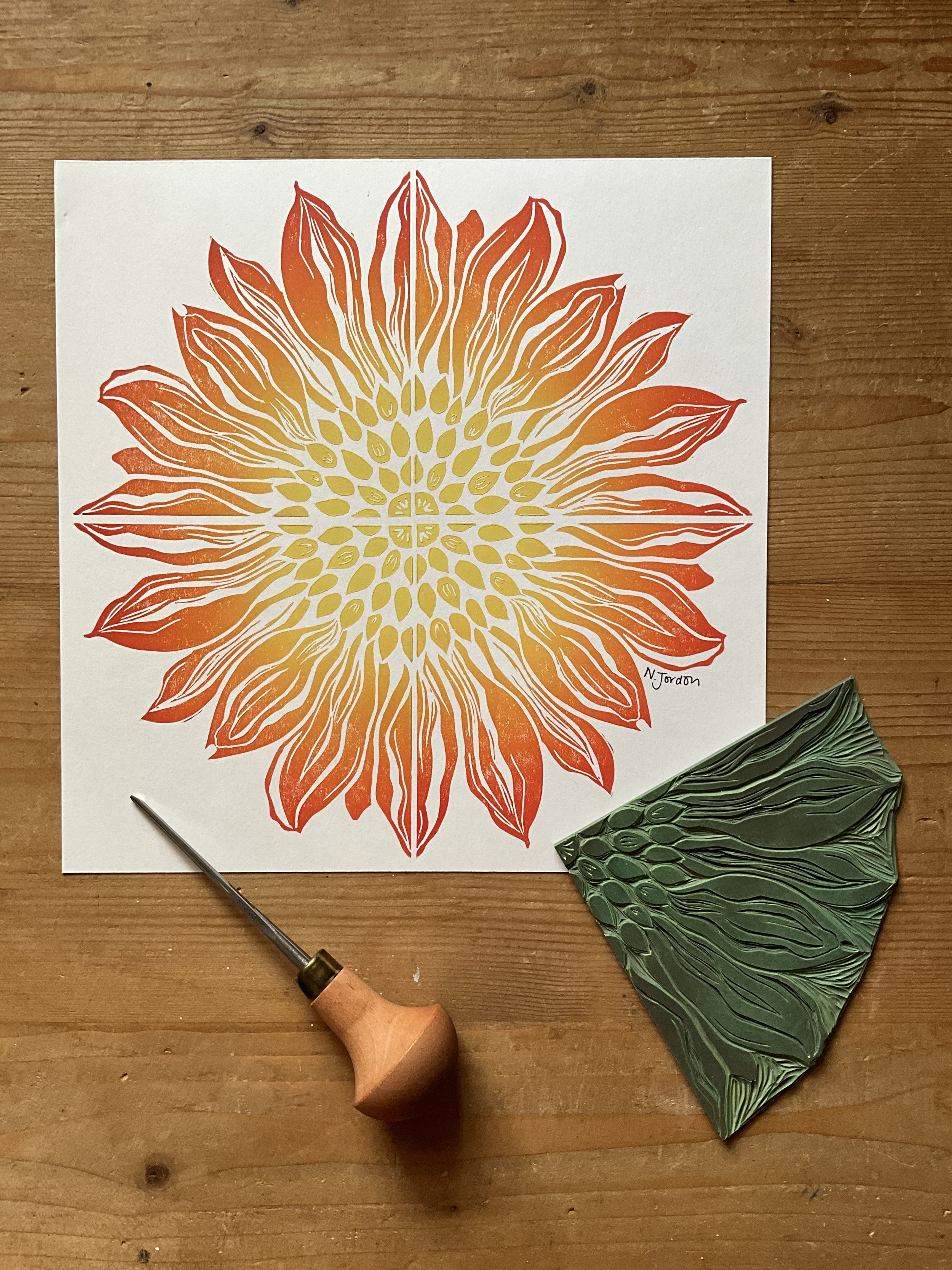 Full sunflower original lino cut print, in A4. Hand printed in orange-yellow ombré. Photo also shows lino carving tool and the sunflower block used to print this piece.