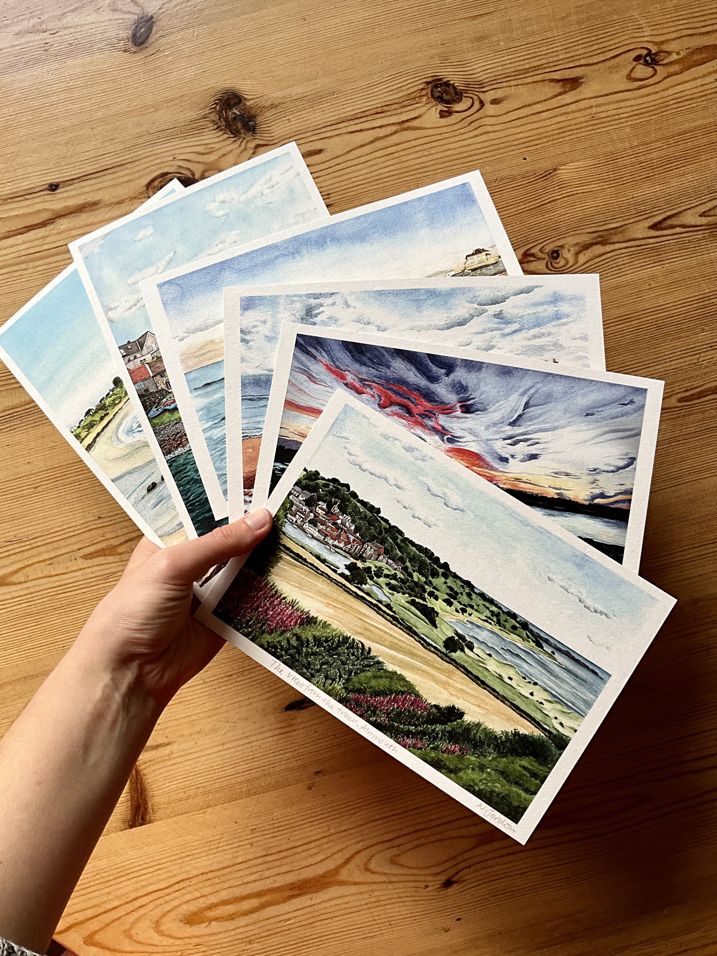 Photo of all 6 landscapes in this watercolour collection, all as A5 art prints and held in my hand as a fan (Copy)