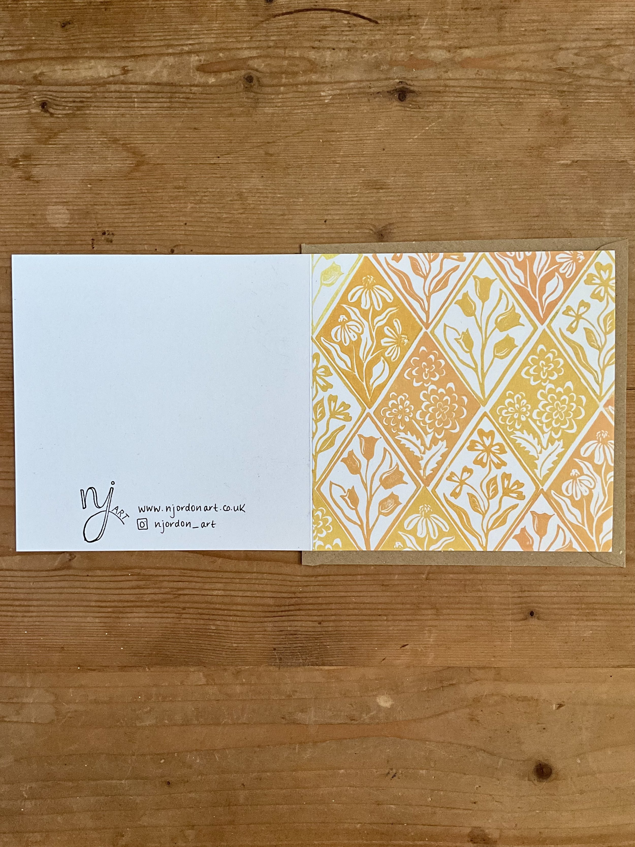 Single square diamond floral greeting card, laid flat to show front and back sides. On top of brown kraft envelope