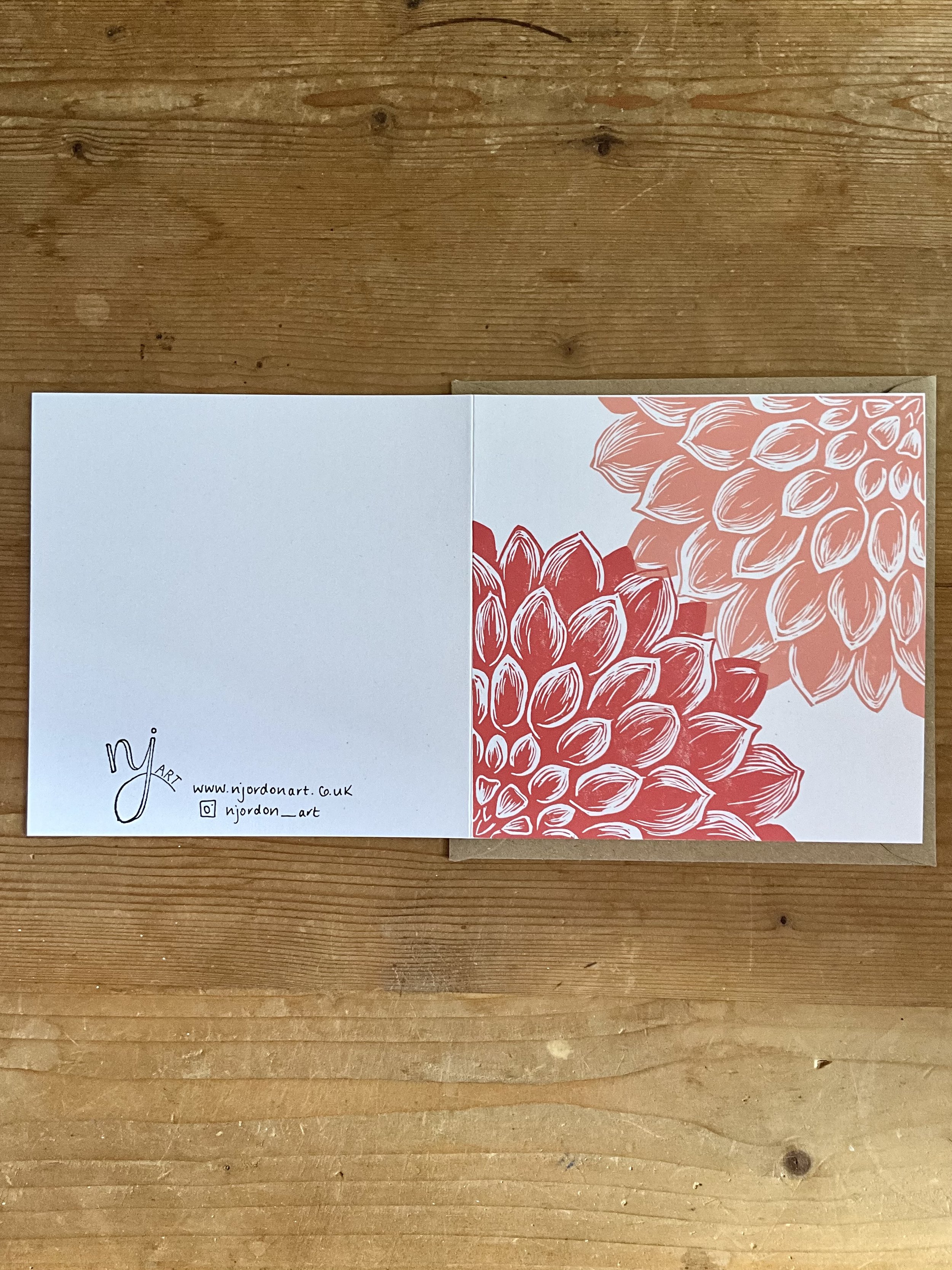 Photo of square dahlia linocut greeting card, laid flat to show front and back of card. Behind is the kraft brown envelope that the card is supplied with