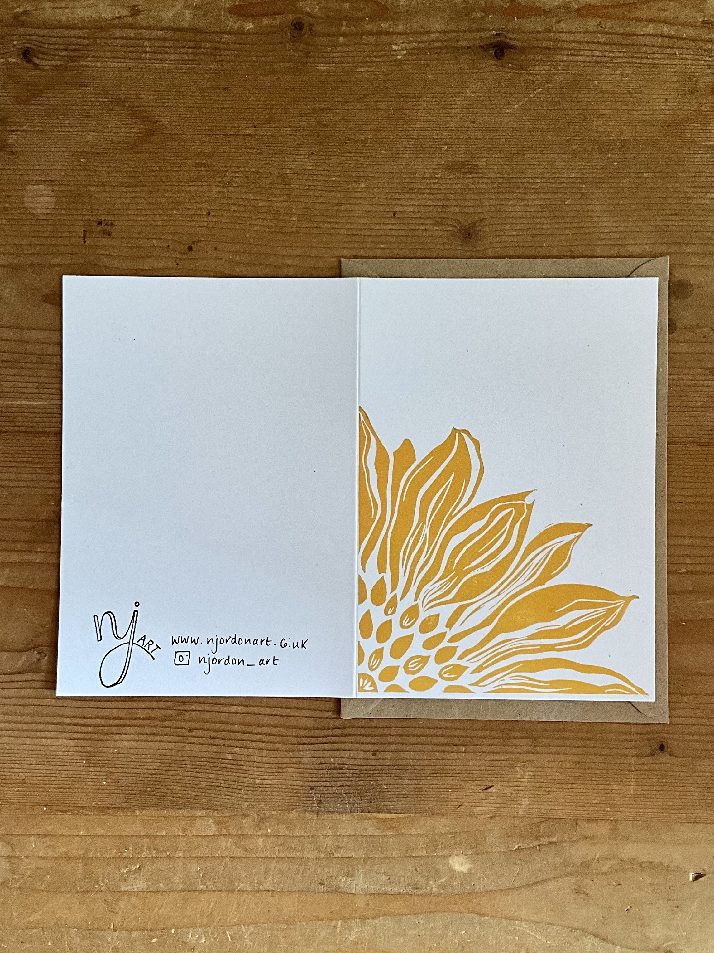 Photo of A6 sunflower linocut card, laid flat to show front and back of the card. Behind is kraft brown envelope