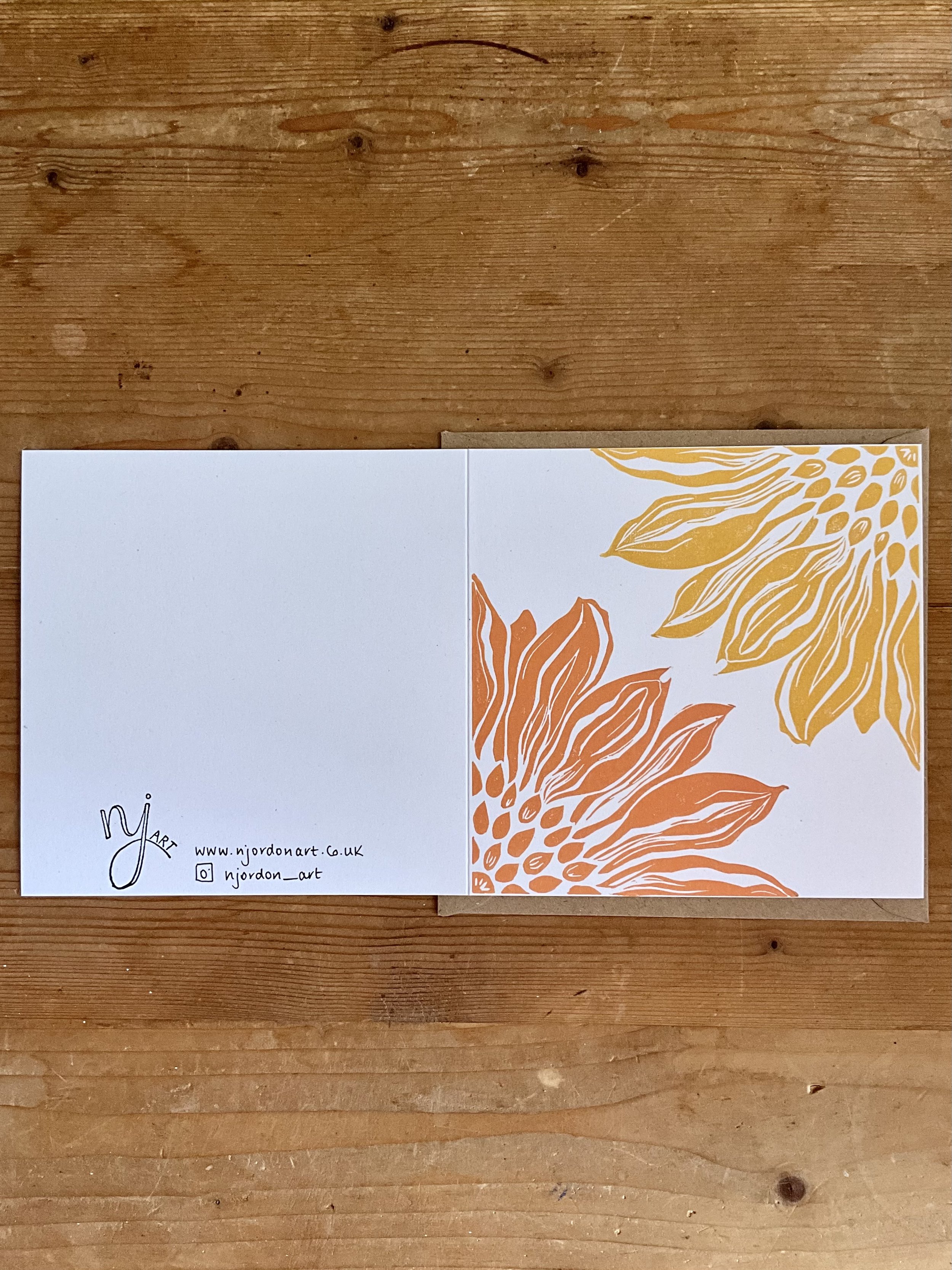 Photo of square sunflower linocut greeting card. Laid flat to show front and back of card. Behind is kraft brown envelope supplied with the card(s)