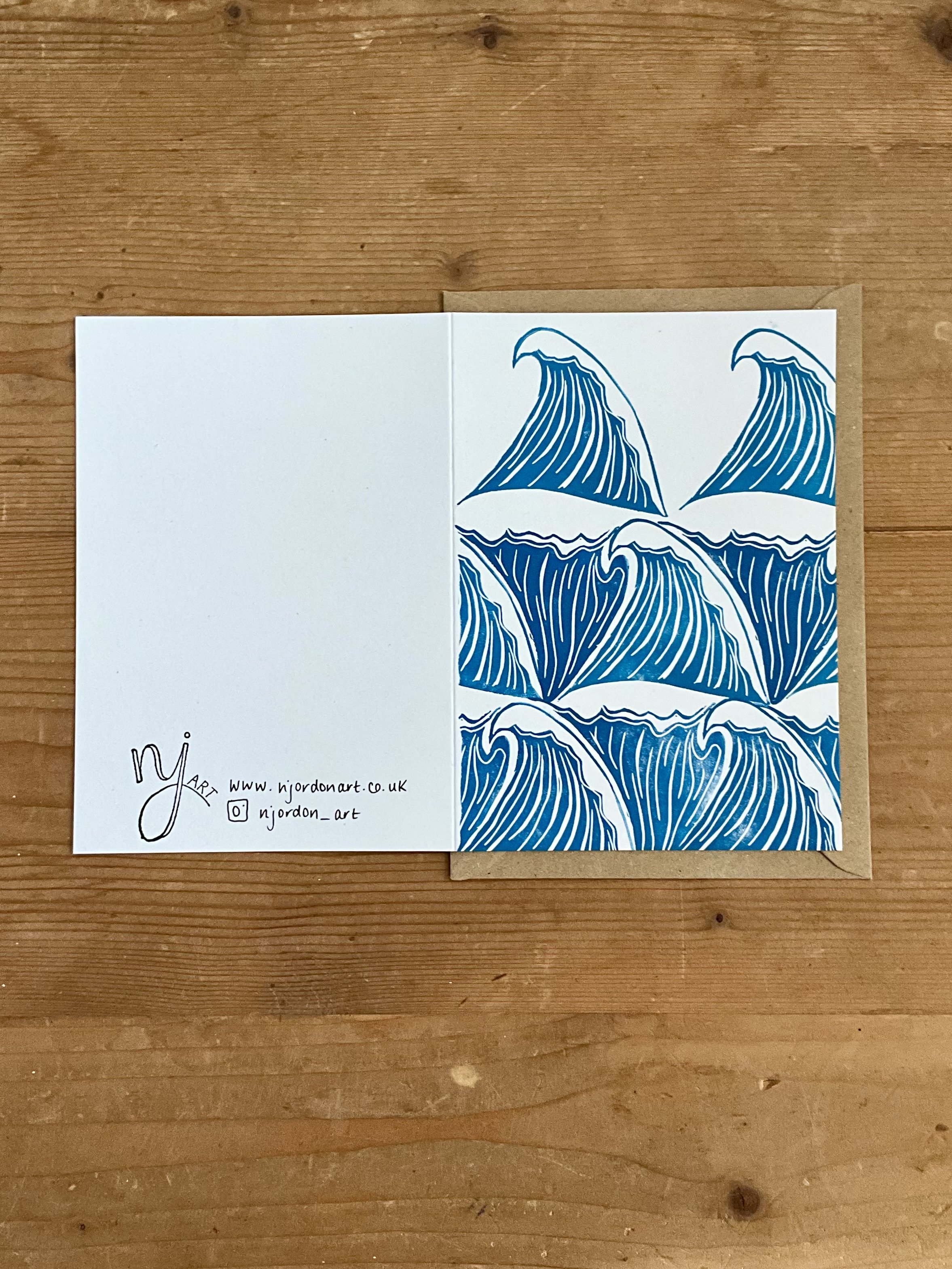 Photo of A6 waves linocut card, laid flat to show front and back of the card. On top of a kraft brown envelope