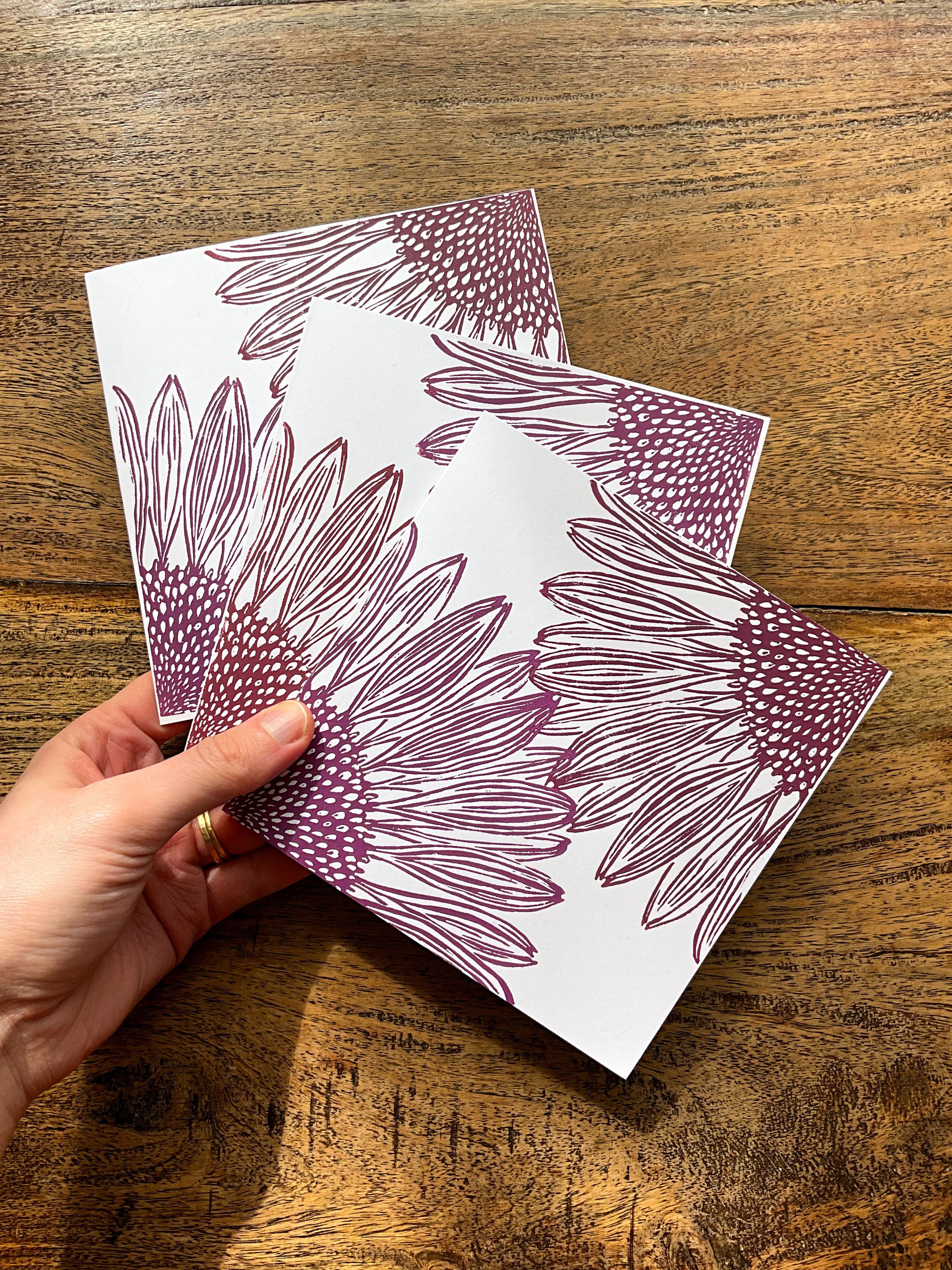 Hand holding three square coneflower linocut greeting cards