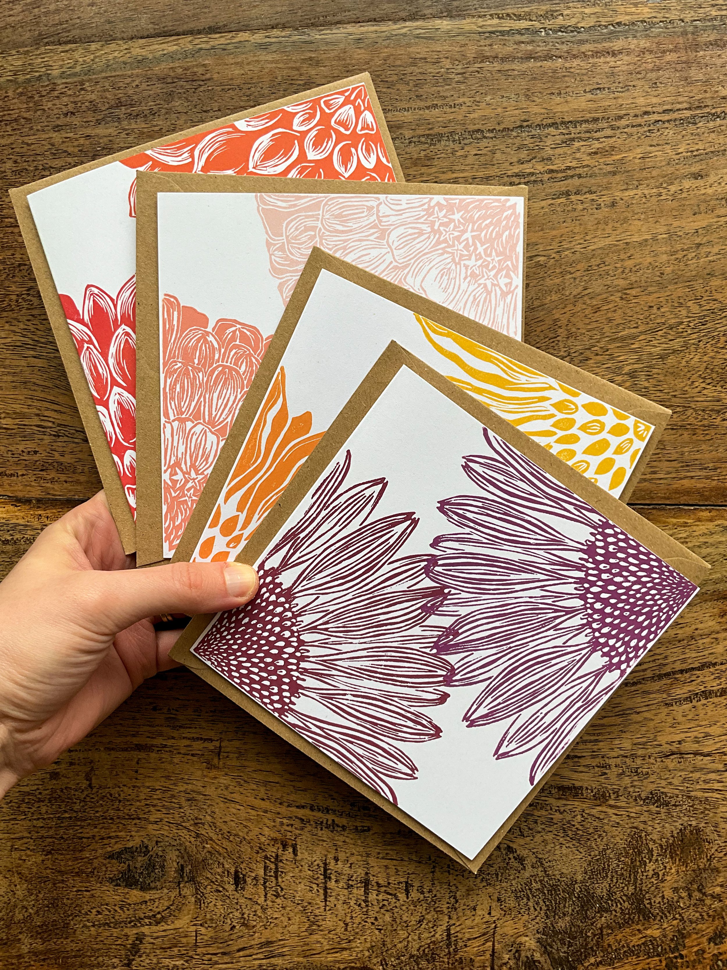 Hand holding four square floral linocut greeting cards, an example of a bouquet bundle.