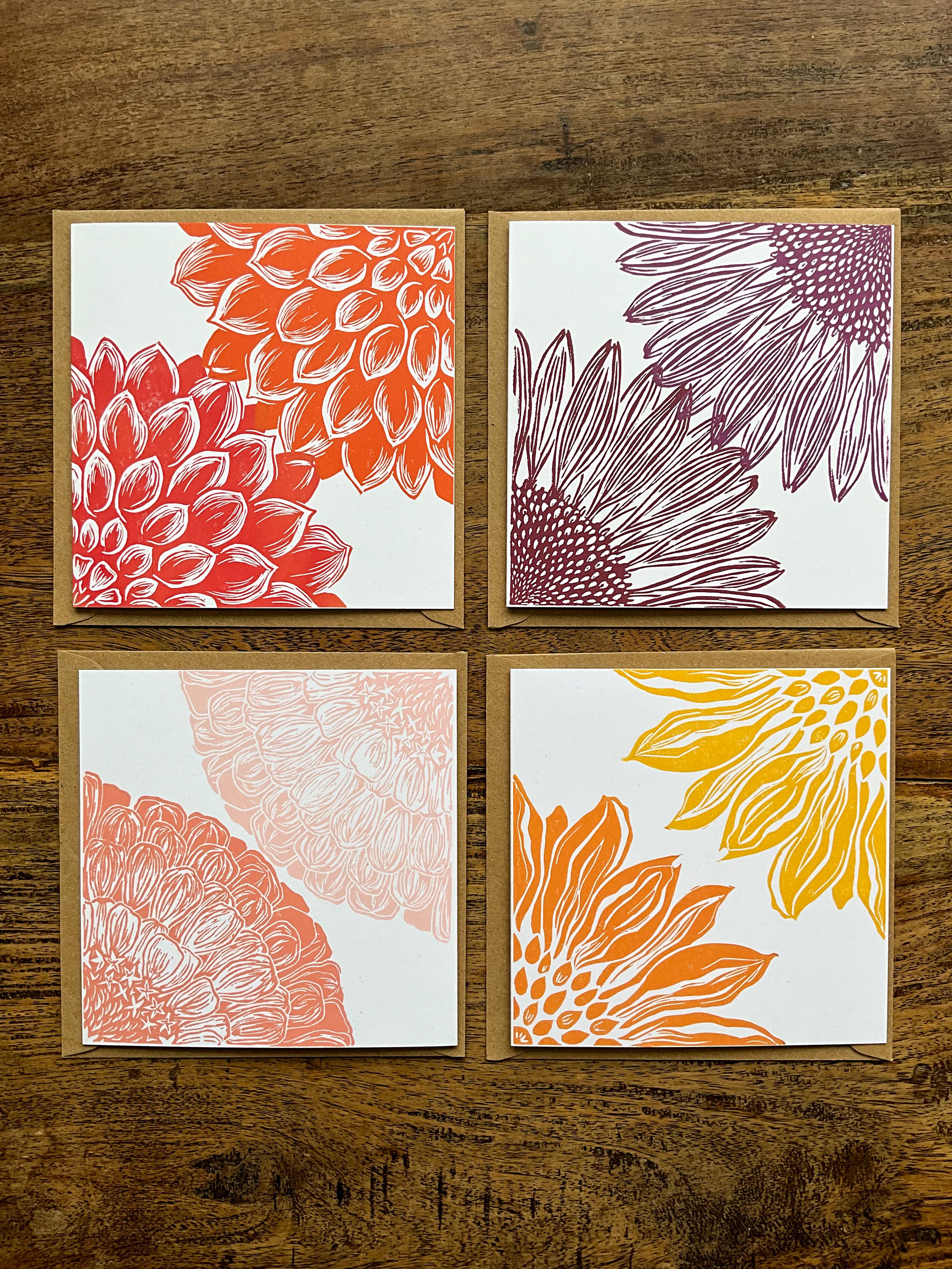 Example of square bouquet bundle of linocut greeting cards. Four square cards laid out on wooden table, each with different design and colours