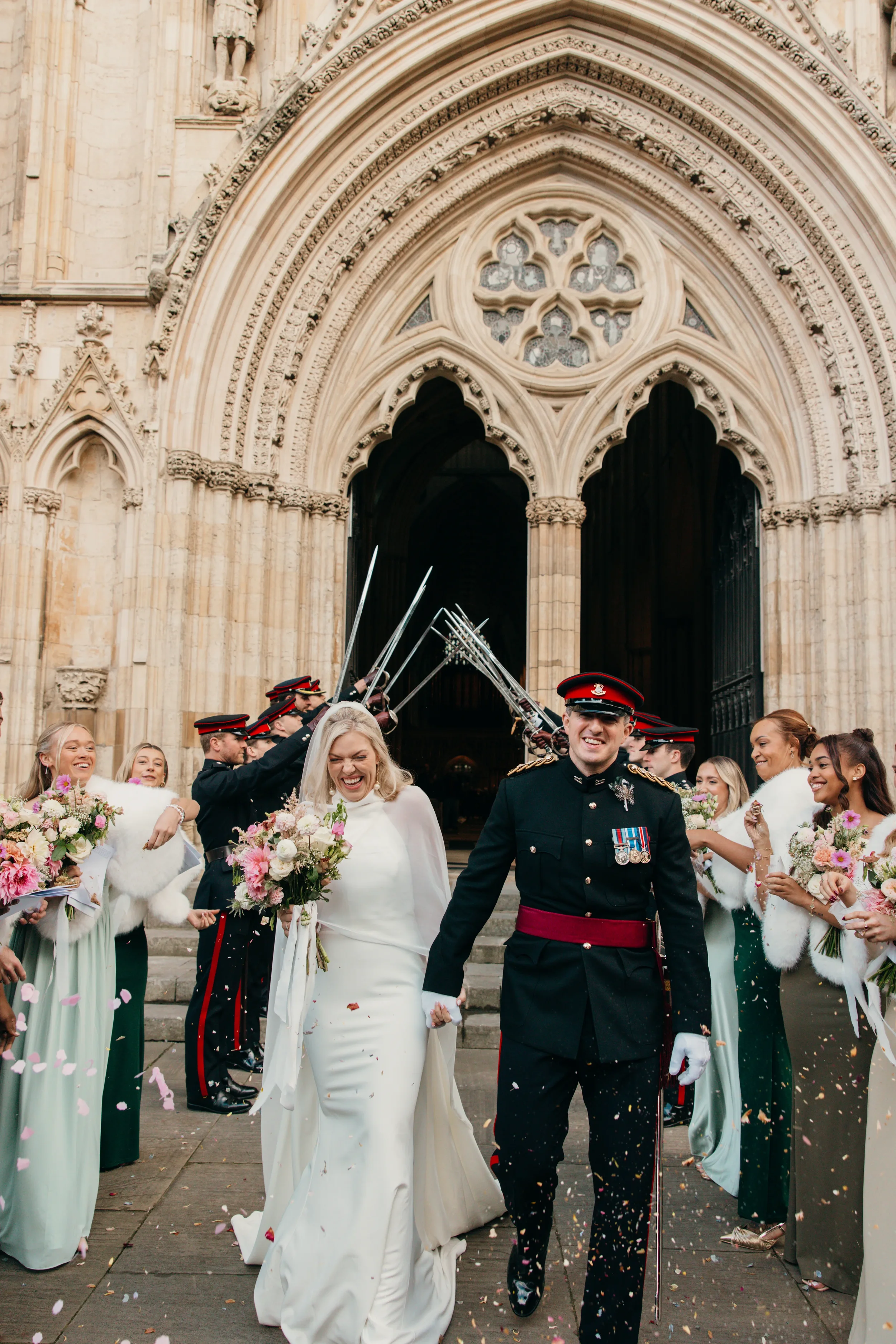 A wedding procession with the bride and groom walking out of a church, surrounded by guests throwing flower petals and confetti.