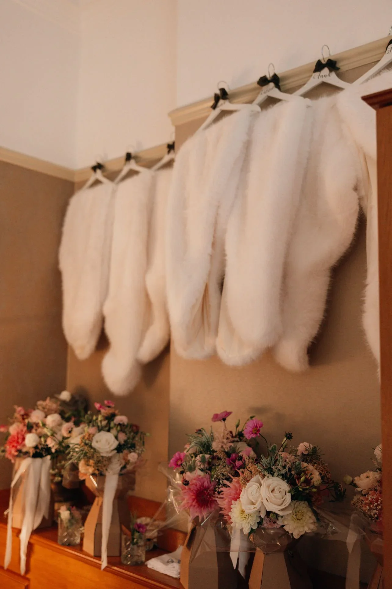 Four white Christmas stockings hang on a wooden rail above a table filled with various bouquets of pink, white, and purple flowers wrapped in clear or decorative paper.