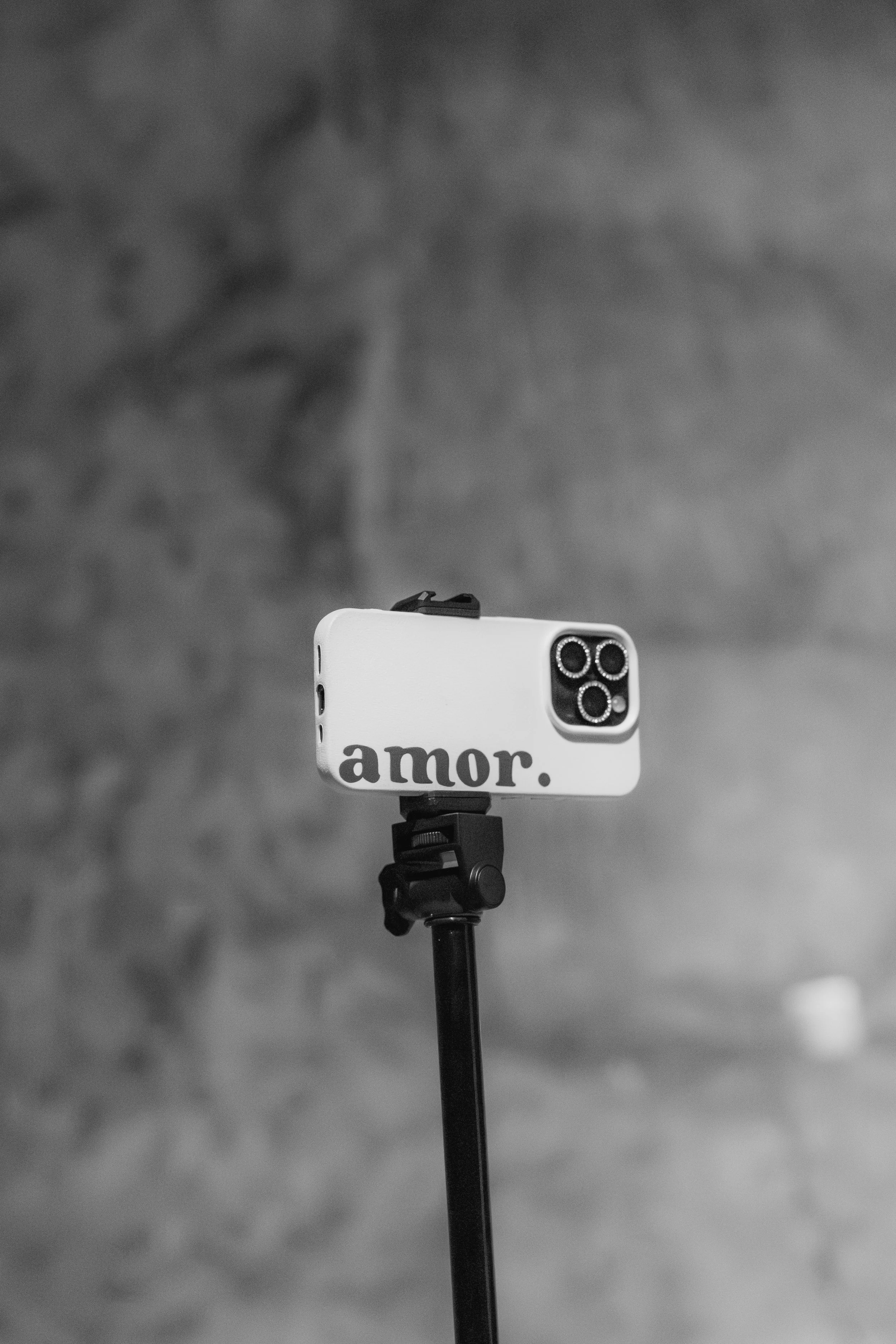 A smartphone mounted on a tripod with the word 'amor.' written on the case, set against a blurred background.
