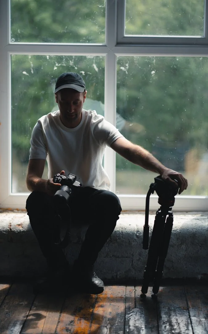 Ben Harrison holding a camera and tripod in a natural light setting