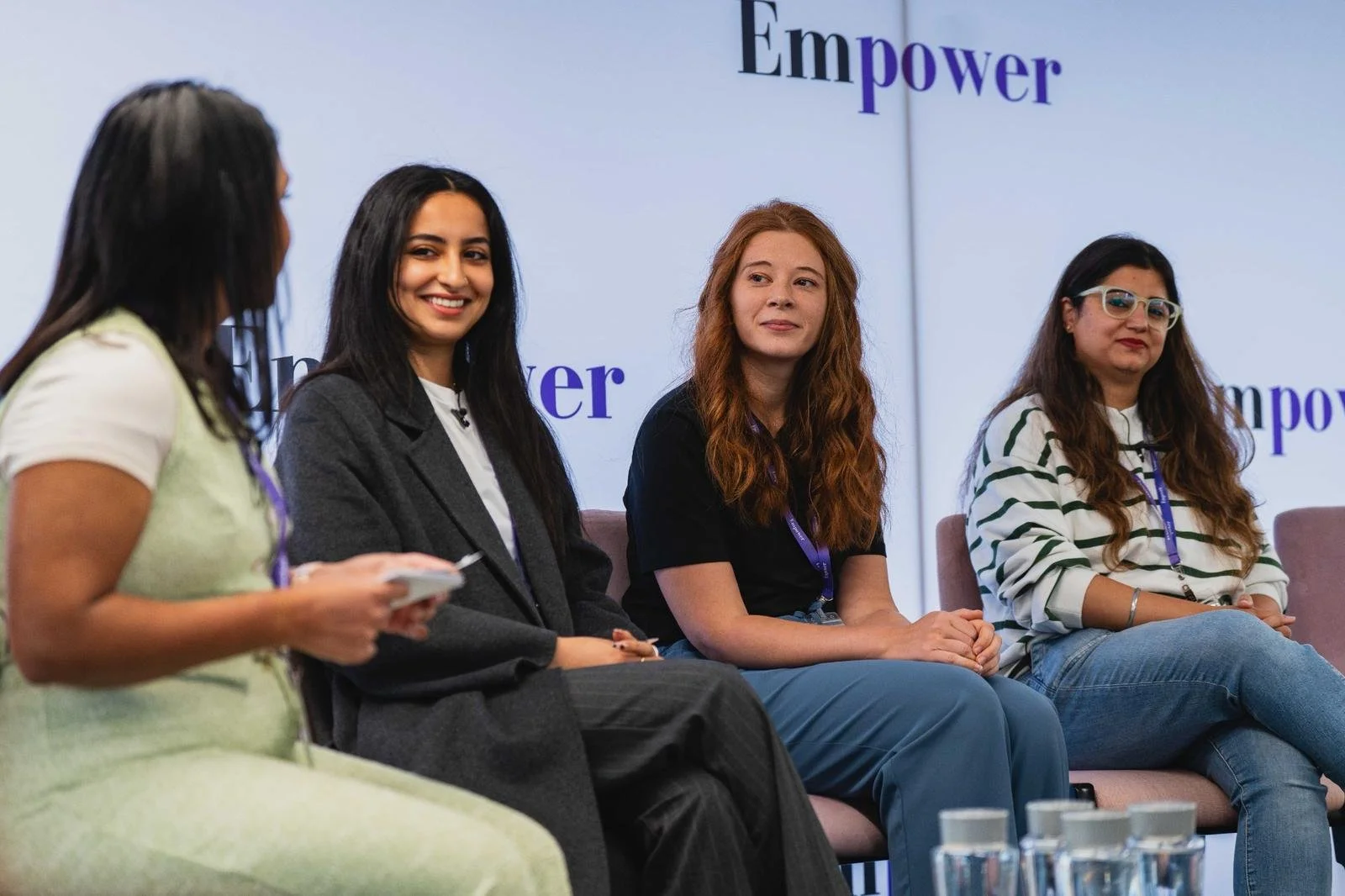 Four women sitting on a panel at an event with a backdrop that says 'Empower'. One woman is speaking while the others listen.
