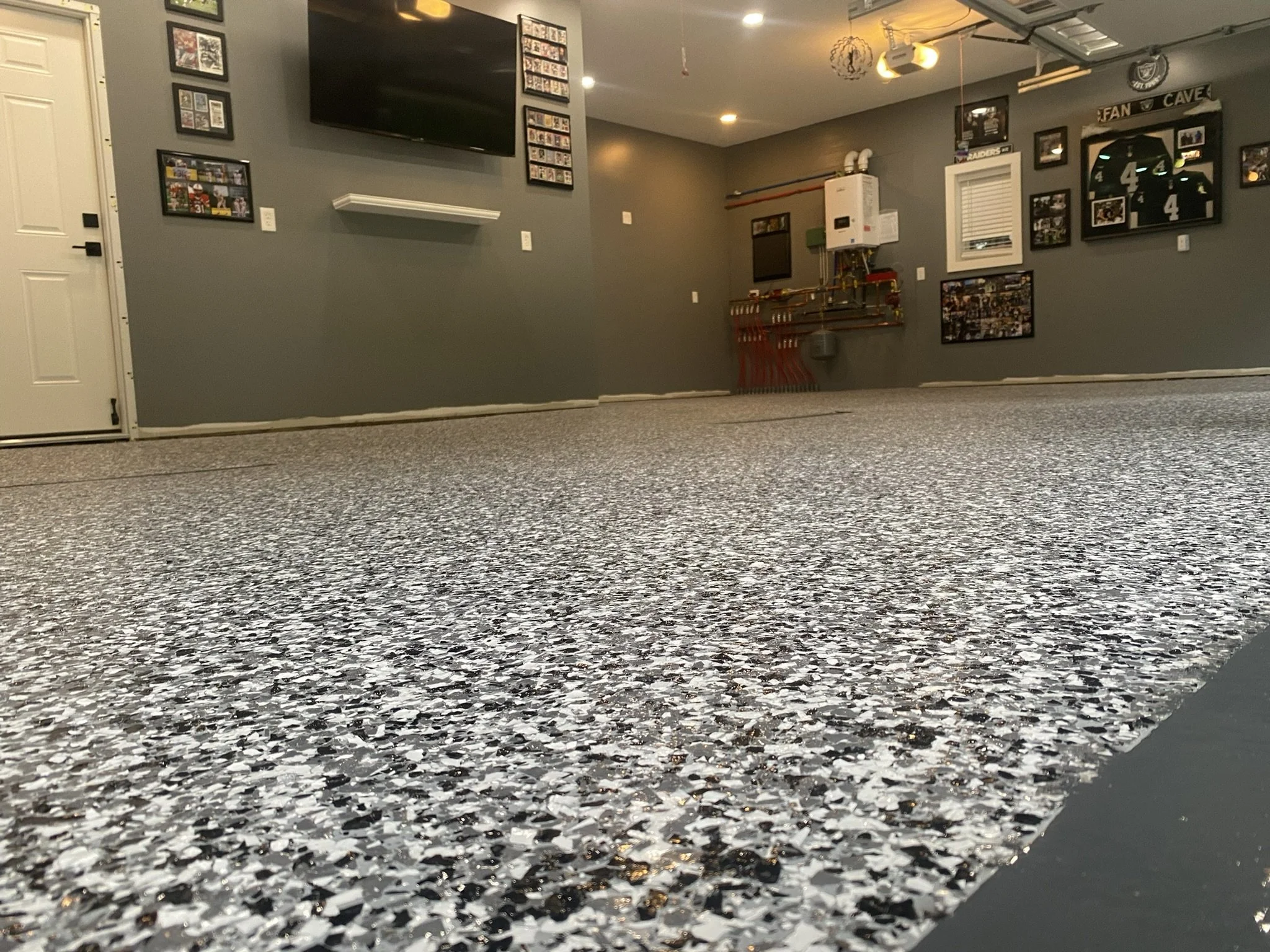 Interior of a garage with a speckled epoxy floor, gray walls featuring sports memorabilia and jerseys, a mounted TV, and a closed white door.