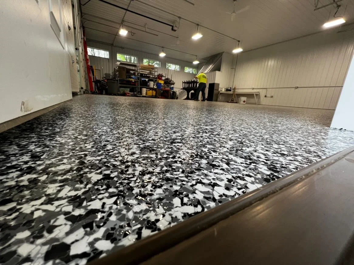 Garage interior with epoxy floor coating, workbenches, and storage shelves.