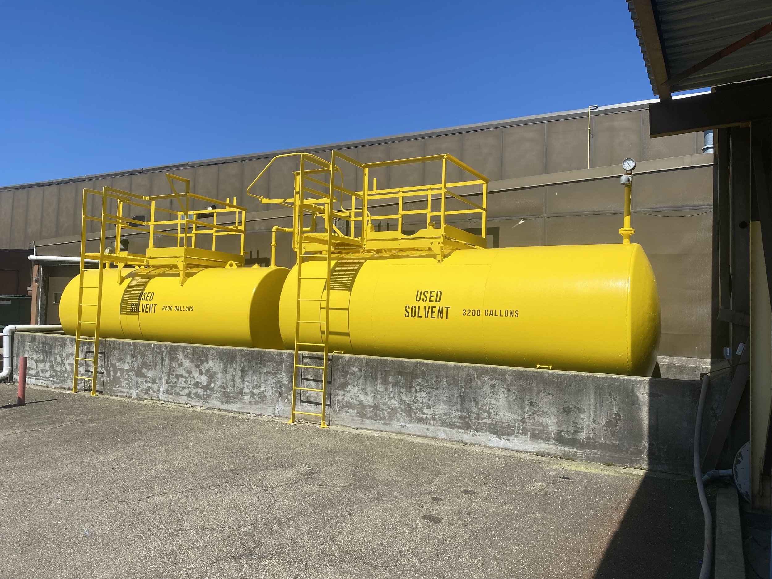 Two large yellow tanks labeled "Used Solvent" with capacities of 2200 gallons and 3200 gallons, situated on a concrete base outdoors.