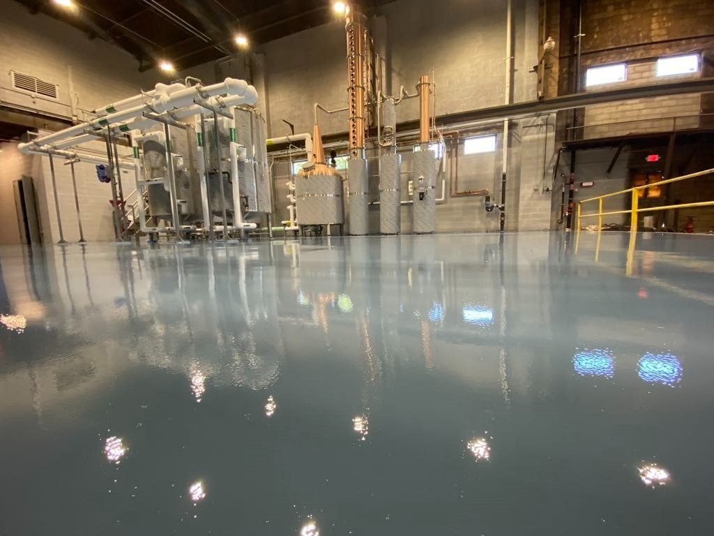 Industrial machinery in a facility with a shiny epoxy-coated floor, featuring pipes and tanks under bright lighting.