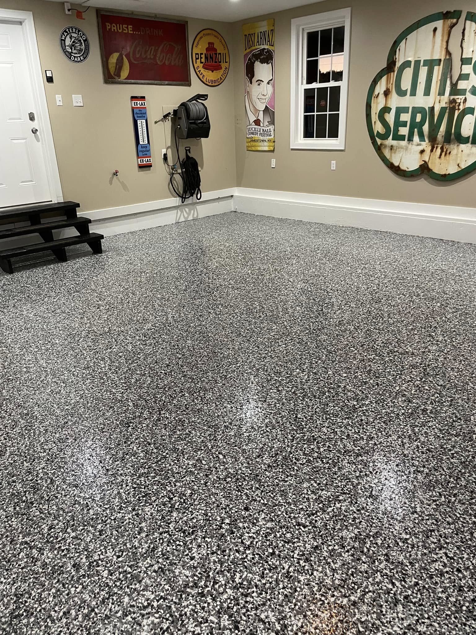 Garage interior with speckled epoxy floor, vintage signs on walls, and coiled hose reel.