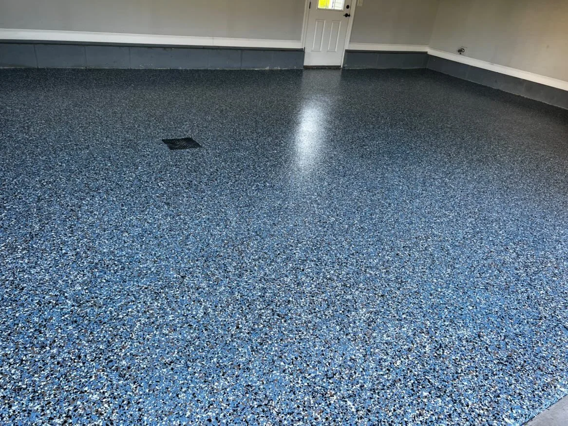 Blue speckled garage floor with epoxy coating and drain, white walls, and a white door.