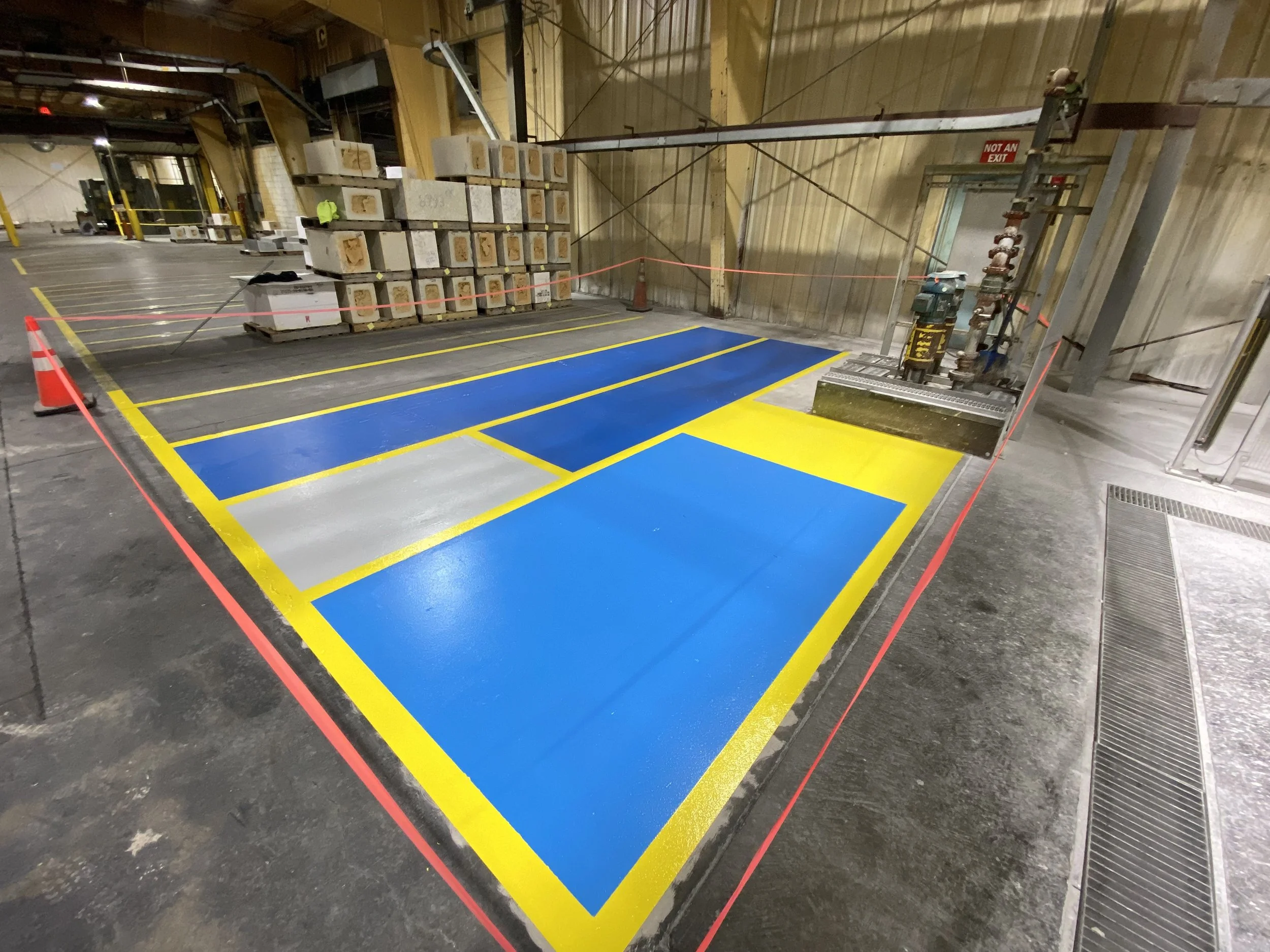 Warehouse interior with painted safety markings, industrial equipment, and concrete blocks on pallets.