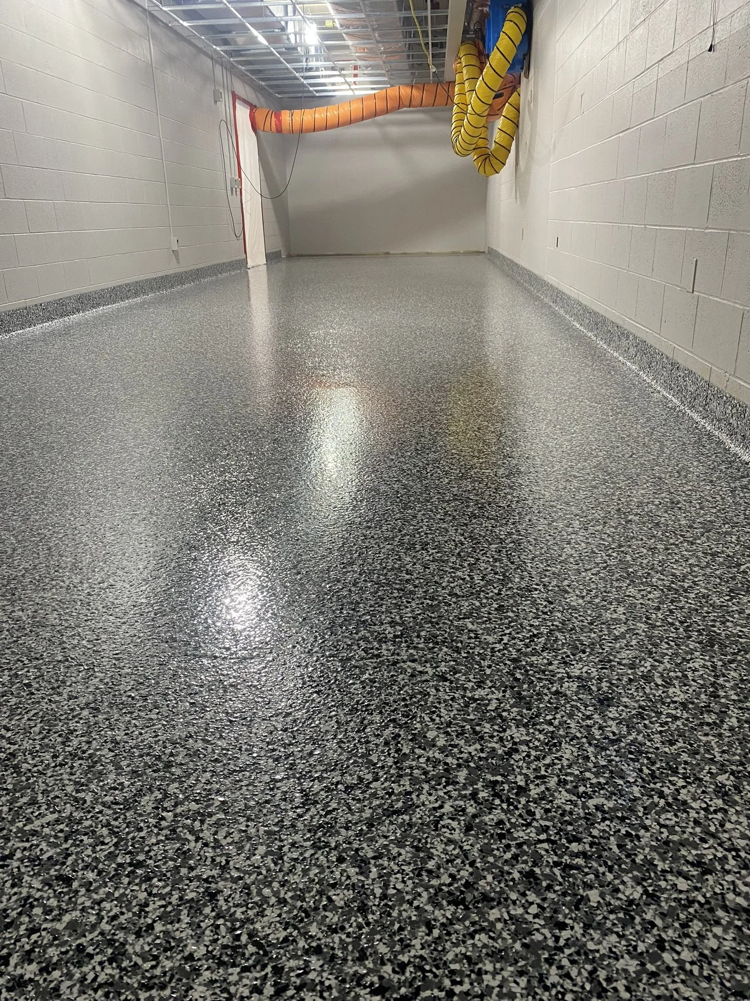 Polished speckled concrete floor in a corridor with exposed ceiling and ventilation ducts.