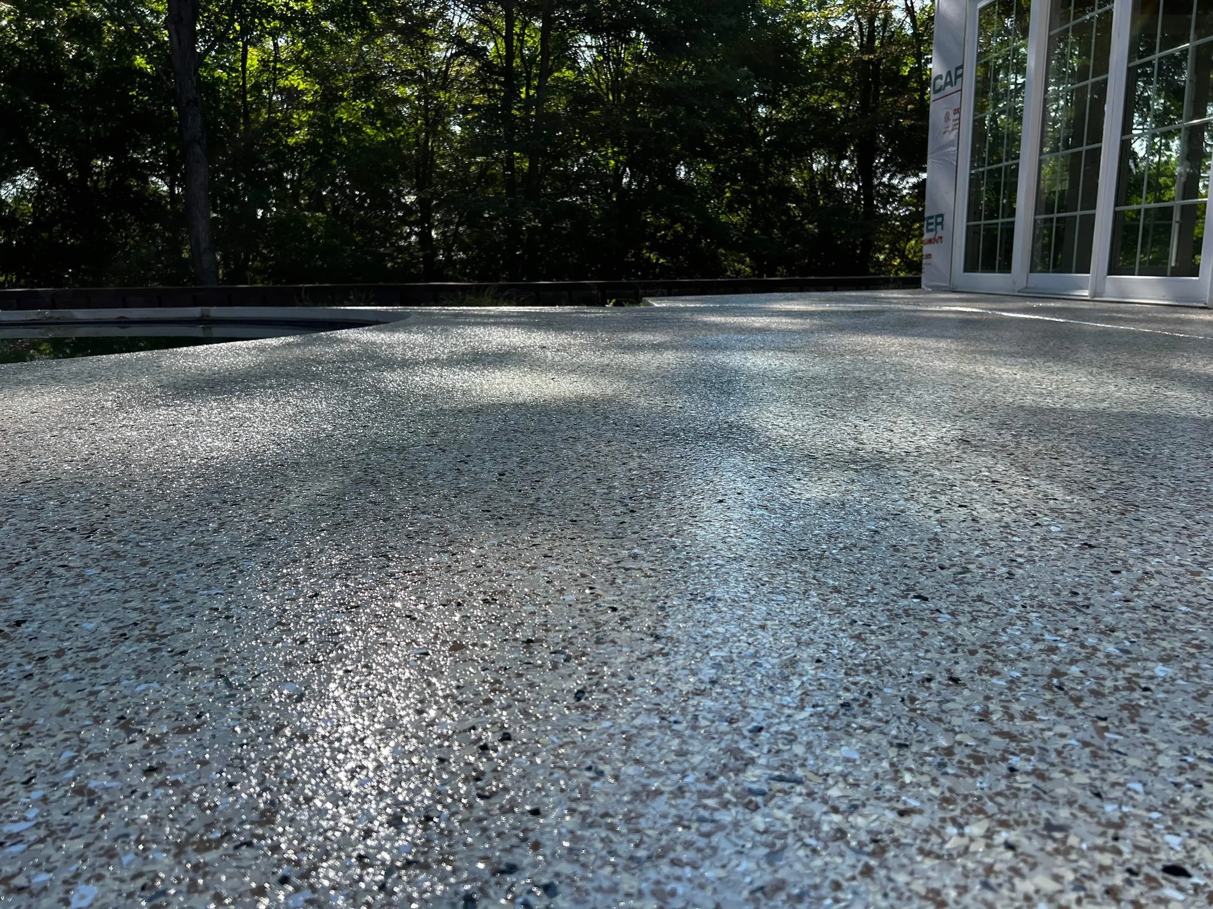 Close-up of a speckled, textured rooftop surface with trees and sunlight in the background.