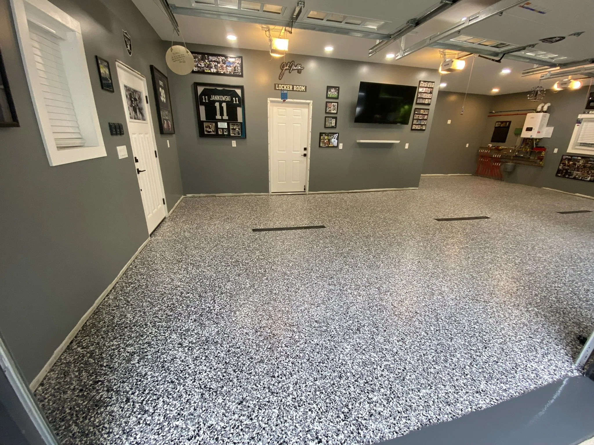 Garage interior with gray walls, sports memorabilia, a mounted jersey, and a speckled floor.
