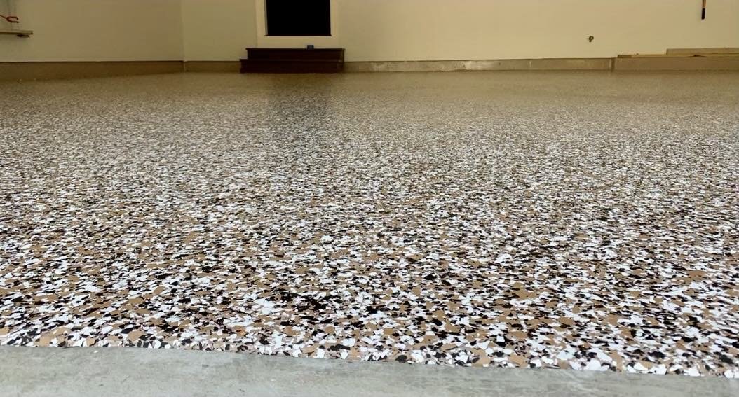 Close-up of a speckled epoxy garage floor in a spacious room with beige walls.