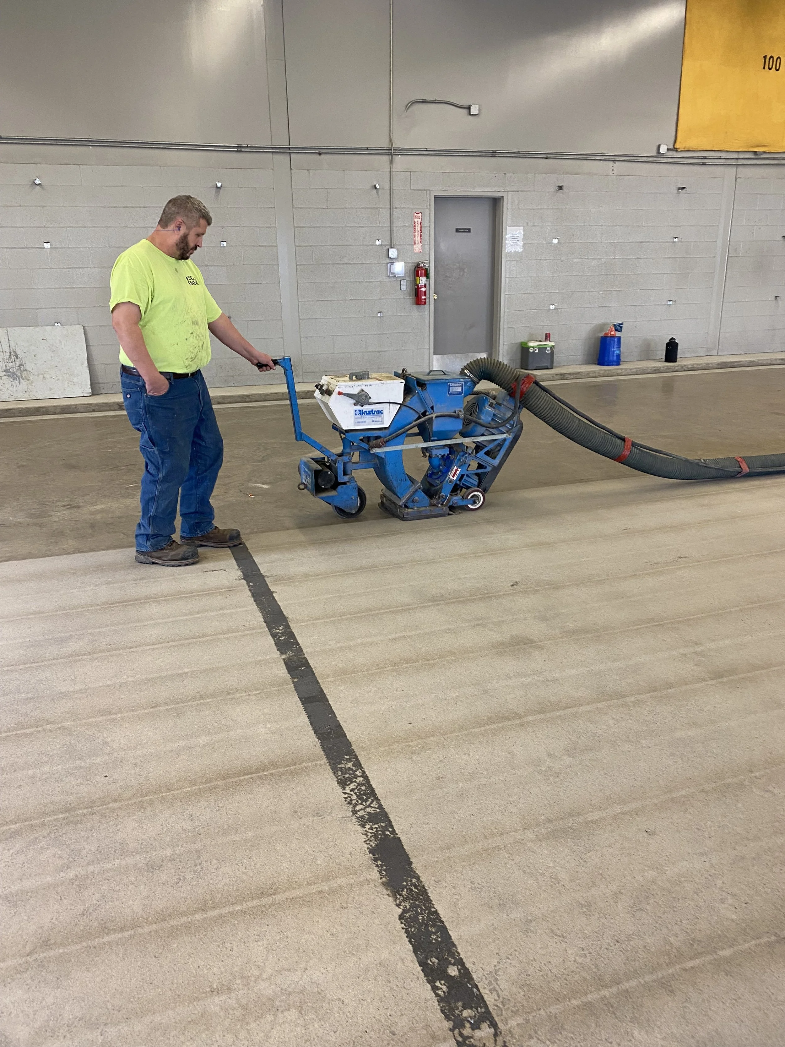Man operating a shot blaster machine on concrete floor in an industrial setting.