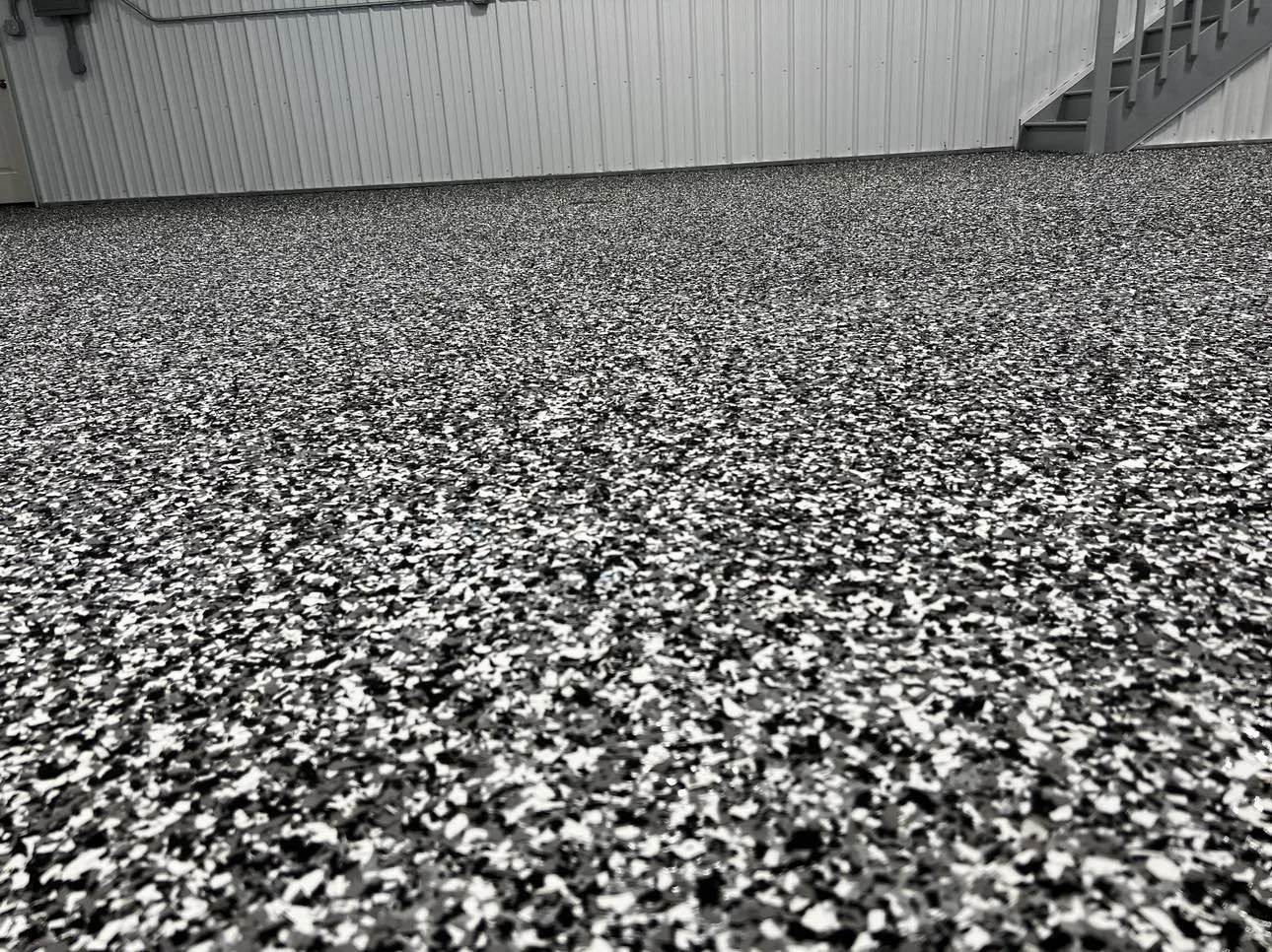 Speckled epoxy garage floor with metal walls and stairs in a bright industrial setting.