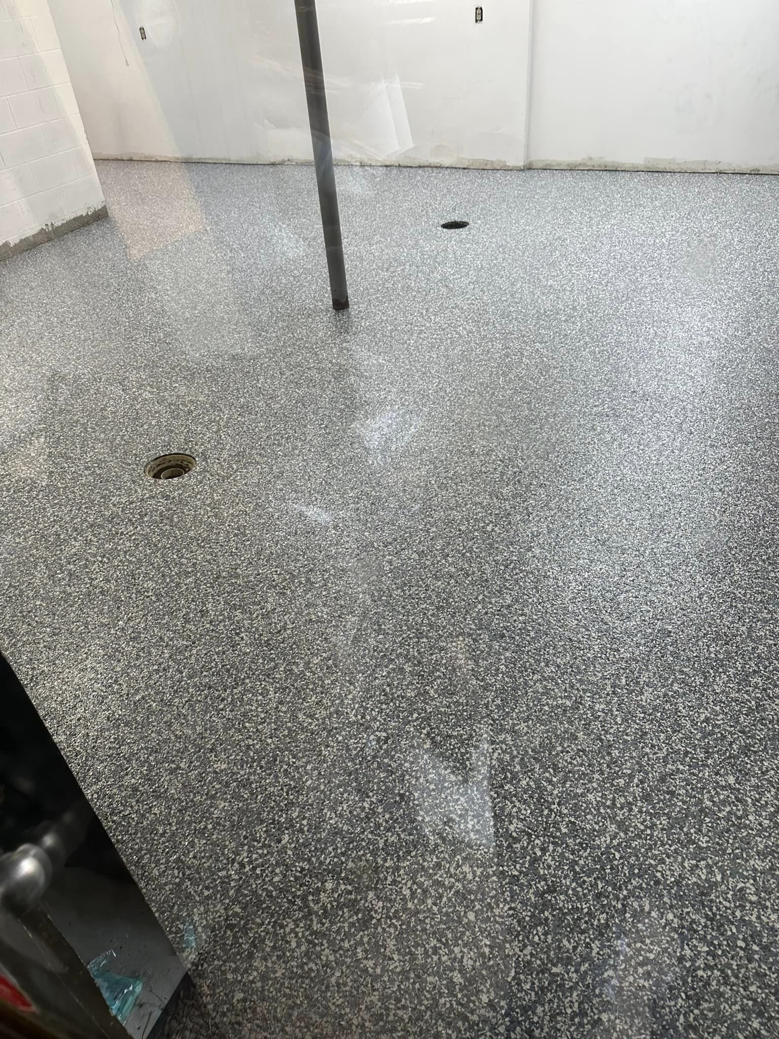 Interior of a room with speckled epoxy flooring, white walls, a vertical metal pole, and two drainage holes.