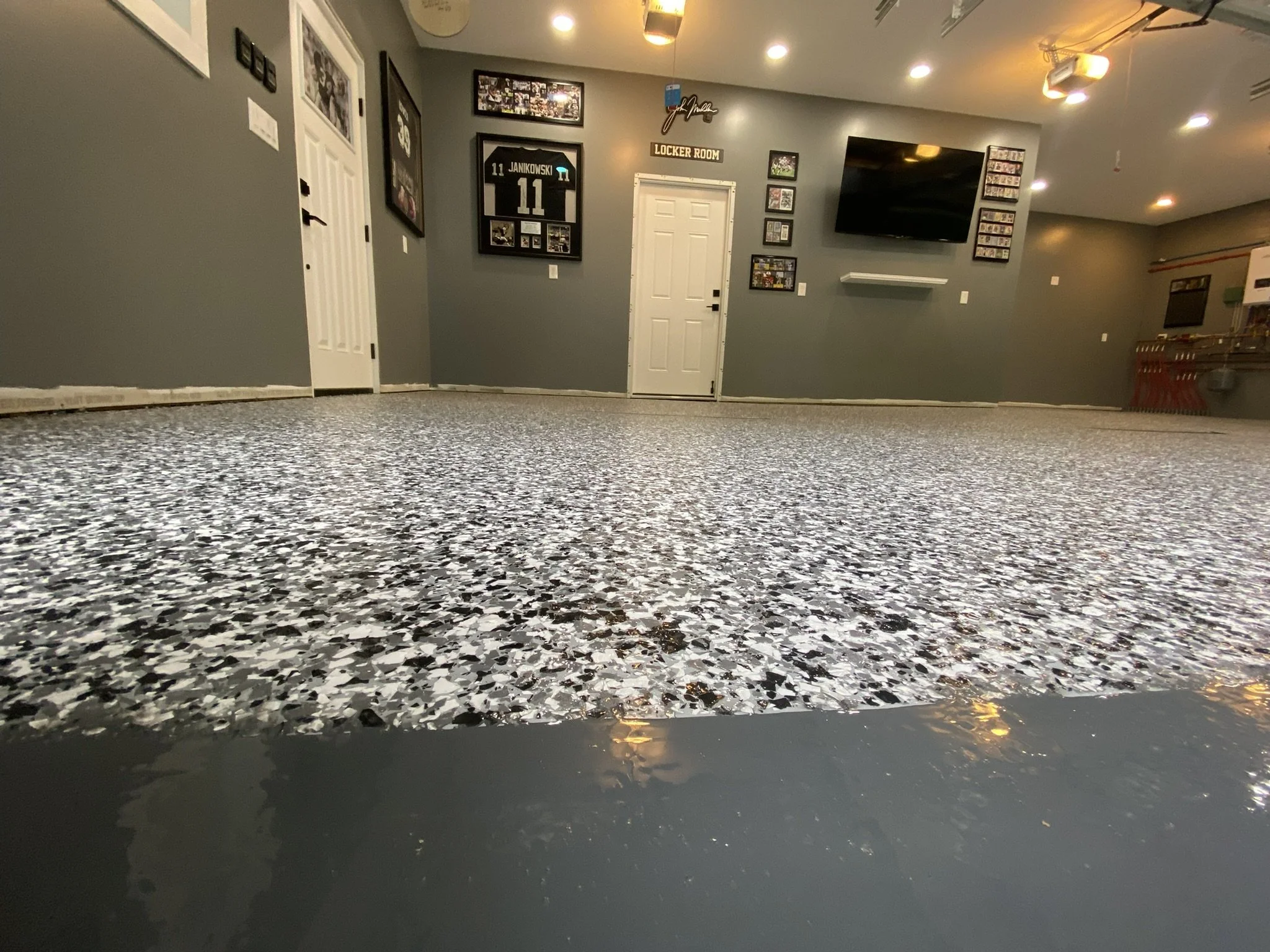 Garage interior with speckled epoxy floor, framed sports jerseys, and a wall-mounted TV.