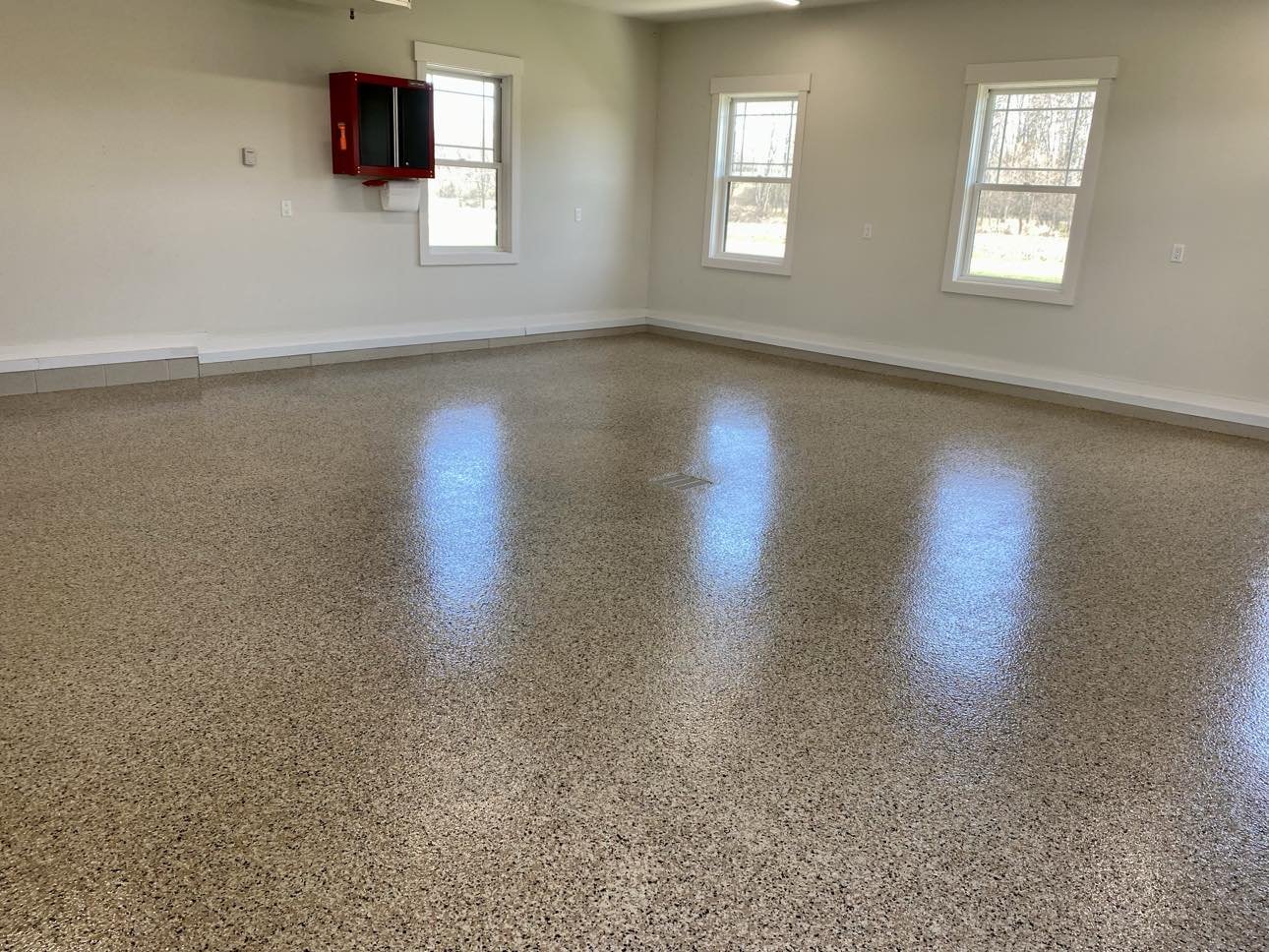 Empty room with polished epoxy floor, gray walls, and windows; red wall-mounted cabinet visible.