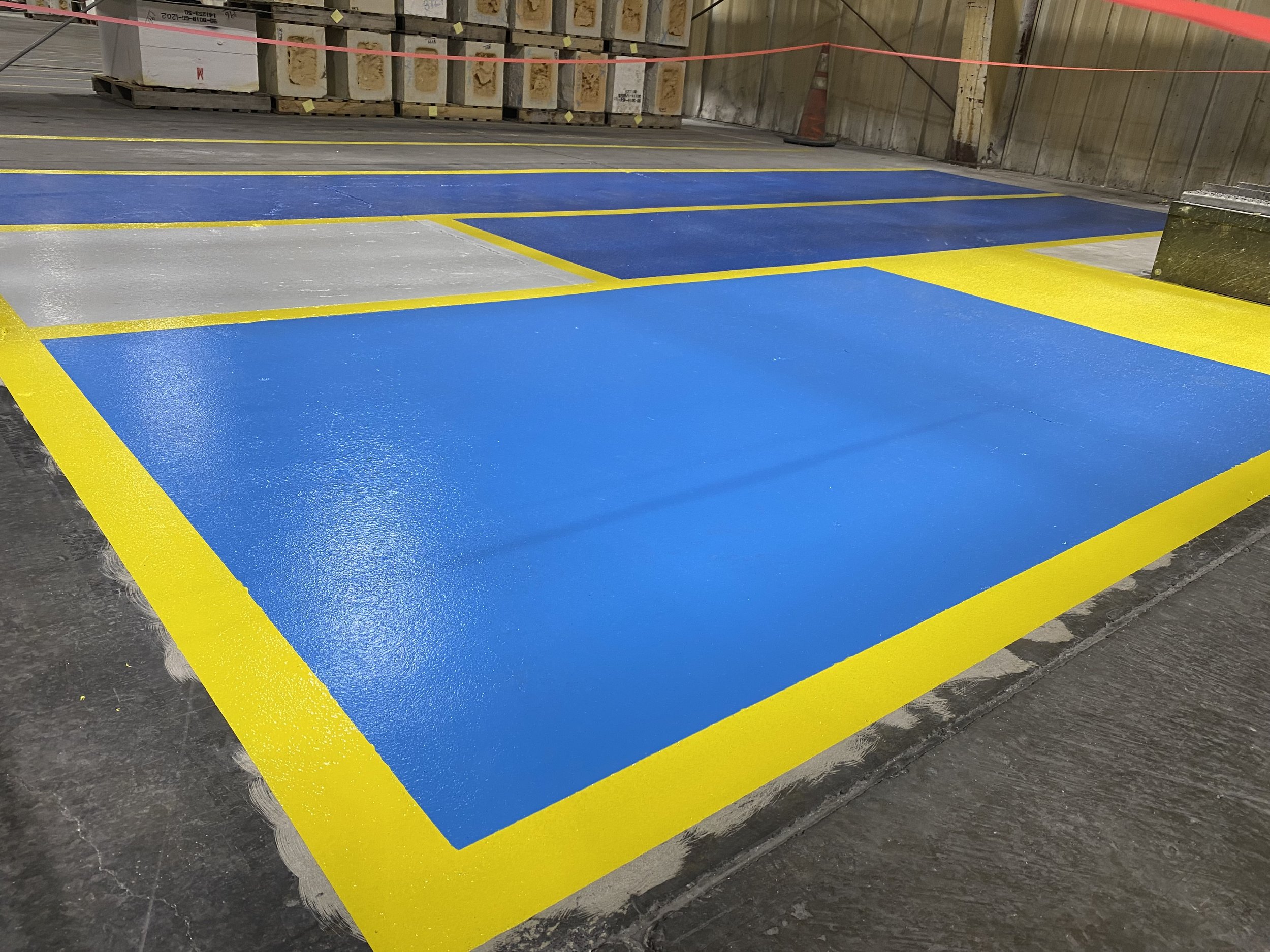 Floor marking in a warehouse with blue and gray colors bordered by yellow lines, used for designating specific areas or zones.