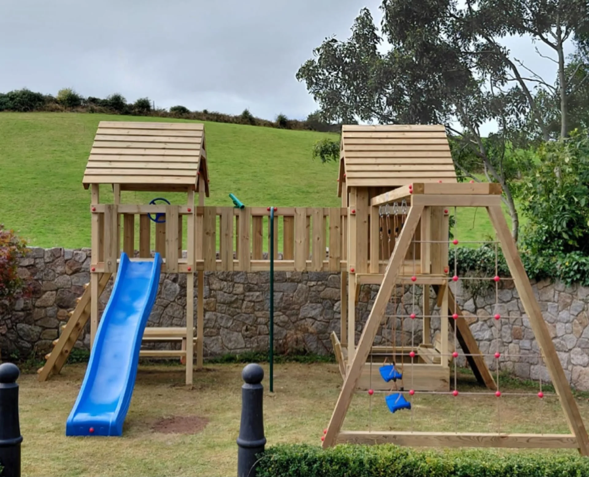 A wooden playhouse with a slide, climbing wall, and swingset in a backyard