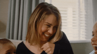 A woman smiling and laughing with a child, sharing a joyful moment indoors.